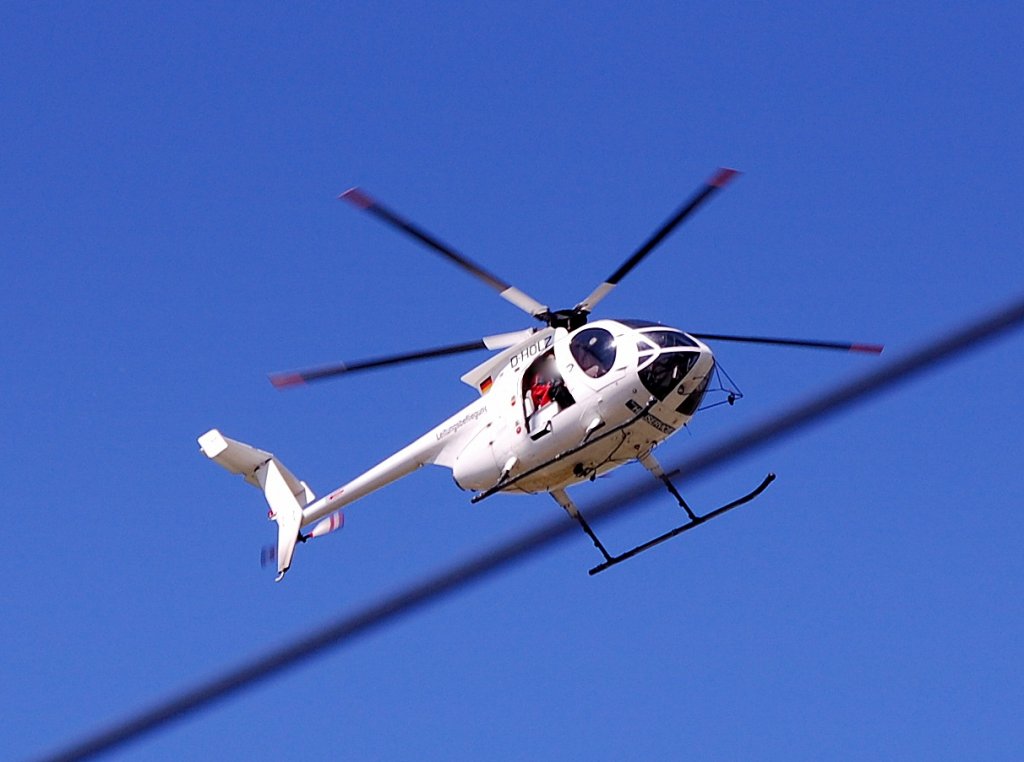 Ein Hughes 369E (D-HOLZ) Helicopter der Fa. Deutscher Helicopter Dienst mit der Aufschrift Leitungsbe(flie?)sichtigung ber dem Bhf. Flughafen Berlin-Schnefeld, 09.05.11.