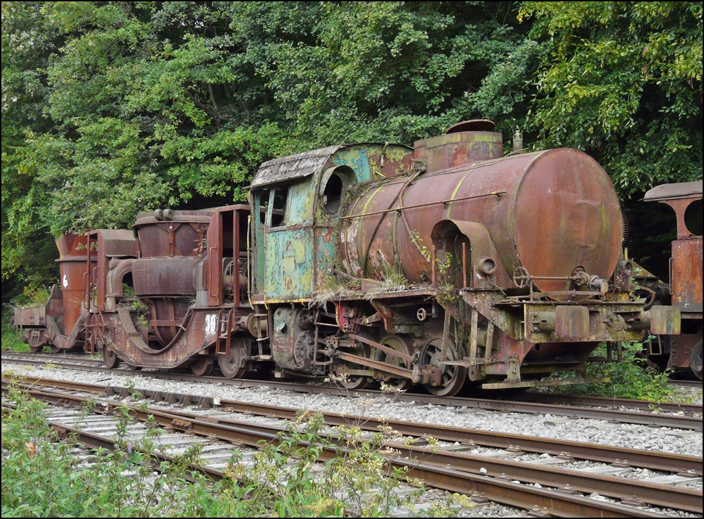. Noch eine Jung Lok in Luxemburg - Bei der Museumsbahn Train 1900 in Fond de Gras warten noch einige Loks auf die Aufarbeitung. Am 13.09.2009 hatte ich die Gelegenheit verschiedener dieser Sch�tzchen abzulichten, unter anderen diese Jung Lok. (Hans)

Die technischen Daten:

Feuerlose Lokomotive V 12, dreiachsig, von ARBED D�delingen
Erbaut im Jahre 1956 von Jung-Jungenthal Kirchen an der Sieg, Fabriknummer: 12513
Typenbezeichnung im Herstellerkatalog:  Felix 
Leistung 250 PS, Gewicht 39 t.

Der Vorteil dieser Bauart ist, dass die Ausf�hrung einfach und robust ist, da das aufw�ndigste Teil im Hinblick auf Konstruktion und Wartung, der Dampfkessel mit seiner Feuerb�chse und seinem Rohrb�ndel durch einen zylinderf�rmigen Beh�lter ersetzt ist. Die F�hrung einer solchen Lokomotive ist entsprechend einfach und erfordert kein qualifiziertes Personal wir die F�hrung eines Dampfkessels. Dem Auspuff der Lokomotive entstr�mt reiner Wasserdampf ohne Verbrennungsprodukte und Russ. Sie kann also ohne Bel�stigung im Inneren von Hallen fahren und auch ohne Gefahr in feuer- oder explosionsgef�hrdeten Bereichen. Der Nachteil liegt nat�rlich in dem eher beschr�nkten Aktionsradius und darin, dass sie auf eine station�re Kesselanlage angewiesen ist. In den Eisenh�ttenwerken, war Dampf sowieso f�r viele andere Prozesse notwendig und daher billig verf�gbar.
