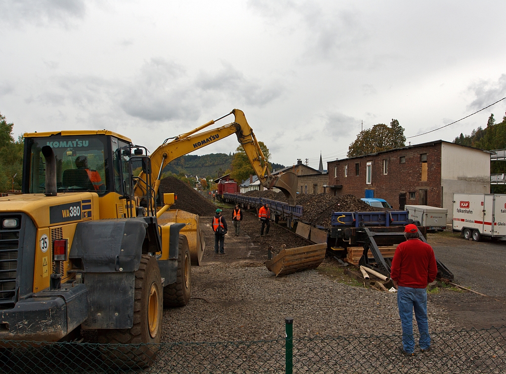 Gleisbaustelle Bf. Herdorf am 14.10.2012 (Erneuerung Gleis 2) - Die V 100.05 (202 726-6) der HGB hat die Res-Wagen mit dem Altschotter auf das Abstellgleis geschoben, nun dr�ckt ein Kettenbager die Bracken (Seitenwandklappen) an, damit die Verriegelunge ge�ffnet werden k�nnen.