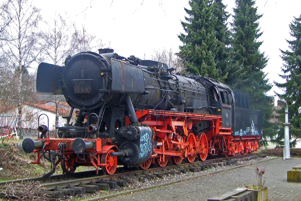 Im meinem Archiv bin ich auf diese Denkmallok gesto�en...

Die G�terzug-Dampflok DB 50 1650 (ex DB 051 650-0) steht am 29.03.2009 noch als Denkmal in Aulendorf, 2010 ging sie dann an den Niederrhein (Stiftung Historischer Eisenbahnpark Niederrhein, Moers).

Die Lok wurde 1942 von Krauss-Maffei unter der Fabriknummer 16193 gebaut und als DR 50 1650 geliefert, nach dem Krieg verblieb sie im Westen und wurde somit 1949 in DB 50 1650 umgezeichnet. Mit der Einf�hrung dem EDV-Baureihenschema der Deutschen Bundesbahn (EDV-gerechten Nummern) erhielt sie 1968 die Bezeichnung DB 051 650-0. 
Die z-Stellung und Ausmusterung erfolgte 1976 im BW Crailsheim, von wo sie dann sp�ter nach Aulendorf als Denkmallok ging.


Allgemeine Informationen zur Baureihe 50

Die G�terzuglokomotiven der Baureihe 50 z�hlen zu den bew�hrtesten Konstruktionen der Deutschen Reichsbahn. Am Ende der Dampflokzeit sind sie zur Universalgattung geworden, die Dank der niedrigen Achslast auch auf Nebenbahnen eingesetzt werden konnten. Bis 1943 wurden 3164 Maschinen der Baureihe 50 von nahezu allen europ�ischen Lokomotivfabriken gebaut. Trotz der Kriegsverluste waren 1945 noch sehr viele Maschinen �brig geblieben. Allein bei der DB wurden nach dem Krieg 2159 einsatzf�hige Lokomotiven registriert. 

Mit der Einf�hrung dem EDV-Baureihenschema der Deutschen Bundesbahn 1968 wurden die Einheits-G�terzuglokomotiven der Baureihe 50, noch 1452 vorhandene Lokomotiven, in die Bezeichnungen 050, 051, 052 und 053 eingereiht, da  die
Ordnungsnummer ja nur noch dreistellig sein durfte. So wurde aus dieser 50 1650 nun 051 650-0, d.h. die erste der vier Ziffern wurde der 50 dazu addiert.  Dies war jedoch nur M�glich, weil es 1968 keine der wenigen verbliebenen Loks der echten Baureihe 52 bei der Deutschen Bundesbahn mehr gab. Sie waren bis 1968 bereits ausgemustert, daher wurde hier keine Umbenennung in Baureihe 052 notwendig.

Die Baureihe 52 („Kriegslok“) war eine „entfeinerte“ Version der Baureihe 50, was f�r Nicht-Spezialisten aufgrund der nahen technischen Verwandtschaft teilweise nur schwer unterscheidbar ist.
Eine einzige Lok der Baureihe 52 gelangte �ber die Deutsche Reichsbahn, nach der Wende, zwischenzeitlich zur DR-Baureihe 52.80 rekonstruiert, in den Besitz der Deutschen Bahn AG und wurde 1993 als 052 134 eingereiht.  Sie ist heute noch betriebsf�hig und im Besitz der Eisenbahnfreunden Betzdorf und steht in Siegen, die 52 8134-0, sie ist eine Rekonstruktion der  DR 52 7138.
Mit dieser Ausnahme ist eine „Zweiundf�nfzig mit f�hrender Null und angeh�ngter Pr�fziffer“ also eine ehemalige „F�nfzig“ aus Best�nden der Deutschen Bundesbahn.
