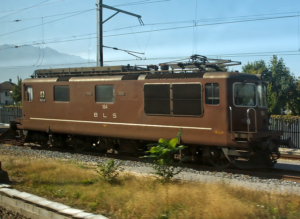 Re 4/4 (Re 425) 164  (Lengnau) der BLS, ex Ae 4/4 II 264, abgestellt am 30.09.2011 bei Bern, fotografiert aus einem fahrenden ICE. 
Die Lok wurde 1967 bei SLM unter Fabriknummer 4636 gebaut. 

Die Loks wurde als Universallokomotive mit guter Bergleistung beschafft, um die Z�ge mit h�heren Geschwindigkeiten bef�rdern zu k�nnen und um die Lokomotiven der Gr�ndungsjahre abzul�sen. Die Dauerleitung der Koks betr�gt 4980 kW (6770 PS).

Die Re 4/4 ist eine Neuentwicklung der BLS und SLM aufgebaut auf die Ae 4/4, der ersten laufachslosen Hochleistungslokomotive der Welt. Das ist an der Kastenform eindeutig zu erkennen, die Einstiege an der Lokfront wurde von der Ae 4/4 �bernommen. Das Fahrgestell ist �hnlich demjenigen der SBB Re 4/4 II. Doch schon da h�ren die Gemeinsamkeiten zu dieser auch sehr erfolgreichen Baureihe auf. So wird die Kraft mit einer anders konstruierten Tiefzuganlenkung und Seilzug auf die Schienen gebracht. Statt Sandereinrichtungen besitzt die Lok Schienend�sen. Bei vielen Versuchen mit z. T. ausl�ndischen Lokomotiven stellt die Re 4/4 noch heute ihre enorme Leistungsf�higkeit am Berg unter Beweis. Einen 630-Tonnen-Zug kann die Lok auf einer 26-‰-Steigung mit 80 km/h bef�rdern. 
