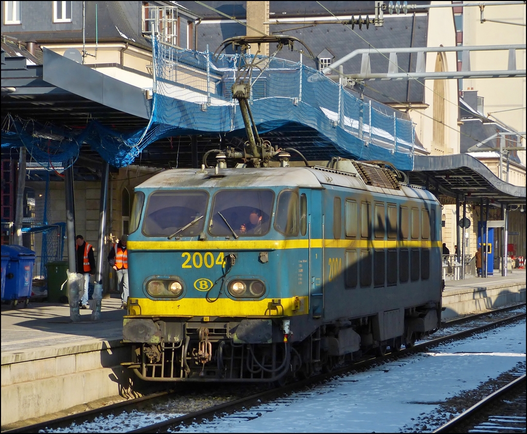 Schon vor einem Jahr lagen dunkle Schatten auf der HLE 2004, auch wenn sie auf dem Bild vom gegen�berliegenden Bahnsteigsdach herr�hren. Die Aufnahme enstand am 01.02.2012 in Luxemburg Stadt, als die tolle SNCB Lok auf den Abstellplatz fuhr, nachdem sie den EC 91 Vauban von Br�ssel nach Luxemburg gezogen hatte. (Jeanny)

Die Loks der S�rie 20 sind mittlerweile fast alle aus dem Verkehr gezogen, einige dienen noch als Reserveloks und ironischerweise muss eine HLE 20 dann einspringen, wenn eine HLE 13 (die nachfolgende Baureihe f�r die EC Vauban/Iris) ausf�llt. 

Die Loks der Baureihe 20 wurden zwischen 1975 und 1978 in zwei Baulosen bei BN (La Brugeoise et Nivelles) in Nivelles gebaut. Der elektrische Teil der Lok stammt von ACEC (Ateliers de contruction �lectriques de Charleroi). Das erste Baulos umfa�te in den Jahren 1975 und 1976 die ersten f�nfzehn Lokomotiven dieser Baureihe. 1977 und 1978 wurde eine zweite Serie mit zehn Loks gefertigt. Als letztes Fahrzeug ging 2025 Anfang 1978 in Dienst. Numeriert wurden die Loks fortlaufend von 2001 bis 2025.

Im elektrischen Teil sind die Loks mit einer Thyristorsteuerung ausgestattet, die aus einem fehlgeschlagenen Versuchsaufbau einer Viersystemlok hervorgegangen ist. Mit ihrer beachtlichen Leistung von �ber 5.000 kW war die Baureihe 20 in der Mitte der siebziger Jahre die st�rkste thyristorgesteuerte Lok weltweit.  Die Loks der S�rie 20 sind derzeit die einzigen 6-Achser im Bestand der SNCB. Die HLE 20 d�rfen nicht in Doppeltration fahren, da ihre Leistung beim Anfahren so gro� ist, dass das Risiko besteht, dass die Halterung zwischen der zweiten Maschine und dem ersten Wagen bricht.

Ihren Einsatz sollten die Loks im schweren Personen- und G�terverkehr finden. Speziell auf der anspruchsvollen Strecke von Br�ssel �ber Namur nach Luxemburg sollte die Lok ihre St�rke ausspielen. 

Der Steckbrief der S�rie 20:

Baujahr: 1975-1978
Nummerierung: 2001-2025
St�ckzahl: 25
Hersteller: BN und ACEC
L�nge �ber Puffer: 19504 mm
H�he: 4185 mm
Dienstgewicht: 	111 t.
Maximale Achslast: 18,34 t.
Dauerleistung: 	5.150 kW
Stromsystem: 3kV Gleichstrom
H�chstgeschwindigkeit: 160 km/h
Achsfolge: Co'Co'
 
