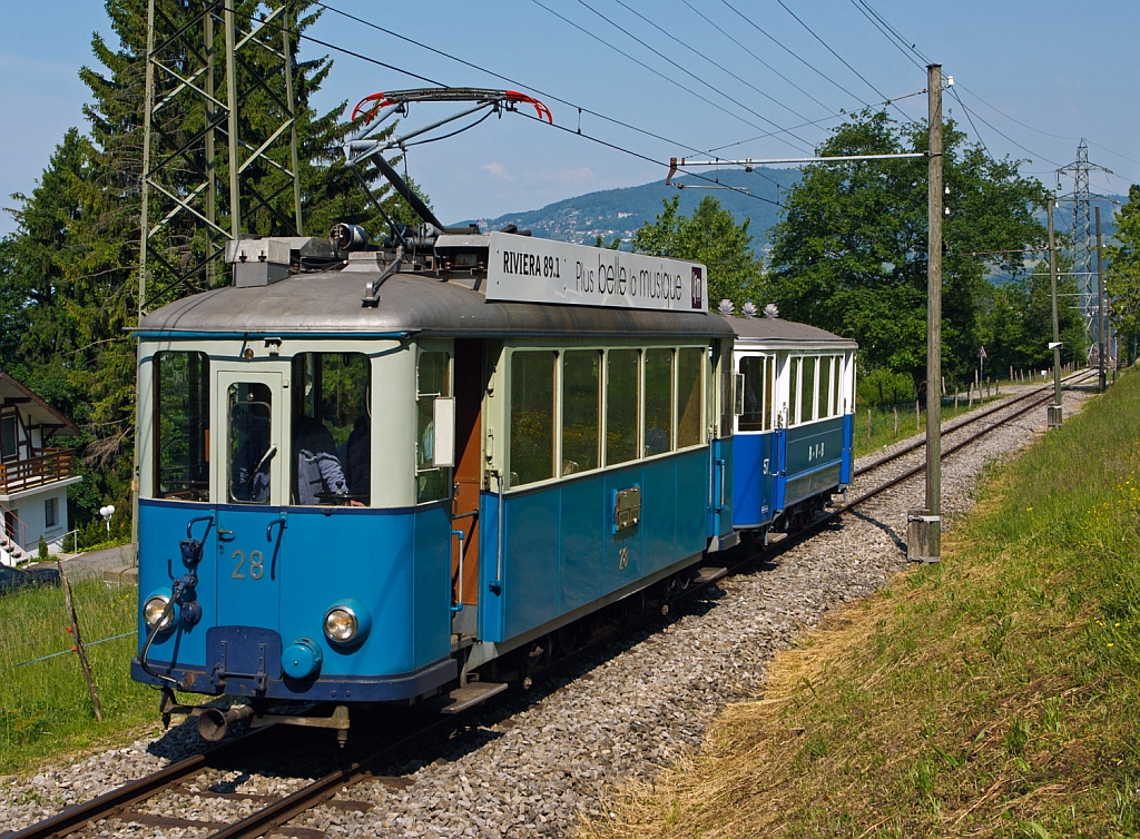 Triebwagen Ce 2/3 ex 28 der TL (Transports publics de la r�gion lausannoise (deutsch �ffentliche Transporte der Region Lausanne)), ex Gen�ve Veyrier 23, BVB 18, dahinter mit dem Steuerwagen Nr. 57 ex BVB (Bex–Villars–Bretaye) kommen von Blonay hoch, hier am 27.05.2012 bei Chaulin. 

Der Triebwagen Ce 2/3 wurde urspr�nglich 1913 als Zweiachser f�r die Gen�ve Veyrier als Nr. 23 von SWS und SAAS gebaut. Bereits 1919 ging er an die TL. Die Werkst�tte der TL baute ihn1948 um, die Aufbauten wurden modernisiert und der Wagen bekam eine zus�tzliche Mittelachse um die Antriebsachsen beim Durchfahren von Kurven zu f�hren. Der Verschlei� wurde somit stark reduziert und der Komfort stark verbessert. 1963 wurde die Jorat-Linie stillgelegt und der Triebwagen, sowie ein weiterer, gingen an die BVB. Der ex TL Ce 2/3 – 28 wurde 1976 an die Blonay-Chamby verkauft und ist eines der letzten �berbleibsel der Lausanner Stra�enbahnen.

Der 8,83 m lange und 5 t schwere 2-achsige Beiwagen wurde 1930 von SIG f�r die VMCV (Transports publics Vevey–Montreux–Chillon–Villeneuve) gebaut. Nach der kompletten Einstellung der Stra�enbahn 1958 (Umstellung auf den Trolleybus Vevey–Villeneuve) wurde der Beiwagen an die BVB verkauft. Lange Zeit war der Beiwagen als Leihgabe bei den TPC, Bahnstrecke Bex–Villars–Bretaye, bis er 2011 als BVB C2 57 zur Museumsbahn zur�ckgekehrte, seit 2013 ist er nun wieder in den urspr�nglichen VMCV C2 57 umbezeichnet. Nun f�hrt er nicht an der Waadtl�nder Riviera, sondern etwas oberhalb.

TECHNISCHE DATEN des Ce 2/3 – 28
Spurweite: 1.000 mm
Achsformel: A 1 A
L�nge �ber Puffer: 11.030 mm
Achsabstand: 2 x 2.100 mm (4.200 mm)
Dienstgewicht: 15.8  t
Treibraddurchmesser: 880 mm (Laufrad ist wesentlich kleiner)
H�chstgeschwindigkeit.:  55 km/h
Leistung: 2 x 88 kW = 176 kW
Getriebe�bersetzung: 1:5,93
Spannung: 900 V DC

