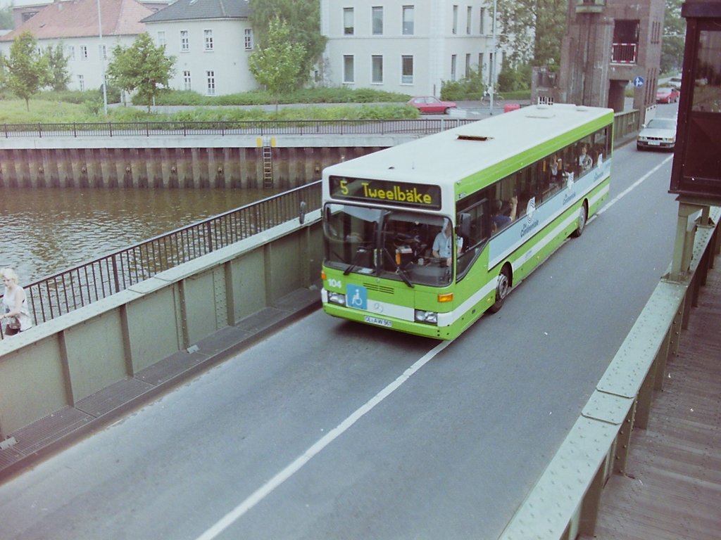 Wagen 104. Ebenfalls im Fahrbetrieb zeigt dieses Bild den Bus auf der Linie 5 beim �berqueren der C�cilienbr�cke in Fahrtrichtung Tweelb�ke. Sowohl die OVB Pekol als auch die VWG hatten �ber Jahre mit den Problemen, die diese Br�cke machte, zu k�mpfen. Eigentlich war der Fahrplan f�r Busse auf der Linie 5 nie wirklich verl�sslich, denn vom Schlie�en der Schranken, �ber das Hochfahren und  Senken der Br�cke und wieder �ffnen der Schranken konnten schon mal 5 bis 7 Minuten vergehen. Manchmal, wenn sich zuf�llig gerade zwei Schiffe im Vorhafen zur Schleuse trafen, oder zwei Schiffe hintereinander fuhren auch mehr Zeit. Die Br�ckenw�rter nahmen leider keine R�cksicht auf die Busse und lie�en diese nicht noch eben passieren. In den 80er Jahren war dies aber manchmal auch geplant, denn die betagte Dame C�cilie blieb auch schon mal beim Herunterfahren wenige Zentimeter �ber dem Fahrbahnniveau h�ngen. Ich hab es mehrmals erlebt, wie dann die Busse vorsichtig auf die Br�cke fuhren um mit ihrem Gewicht die  C�cilie  in ihre vorgesehene Position zu dr�cken. Auf Dauer war dies nat�rlich kein Zustand und die Streckenf�hrung musste ge�ndert werden. Zudem war die Br�cke auch nicht mehr auf die regelm��ige Benutzung durch die Busse ausgelegt. Die 
Fahrbahn war, wie auf dem Bild zu sehen ist, zu eng und die sich h�ufenden Totalausf�lle zerrten an den Nerven der Fahrg�ste und der Fahrer. Mit der Fertigstellung der hochgelegten Amalienbr�cke im Jahr 1980 wurde die Streckenf�hrung der Linien 5 und 12 daher zun�chst verlegt. Sp�ter fuhr die Linie 5 dann wieder auf der alten Route.