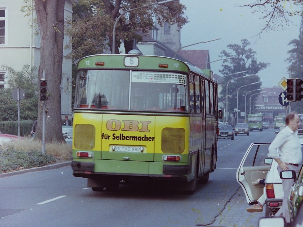Wagen 12, OL-AC 982, EZ: 1976, aufgenommen in der Peterstra�e am 02.10.1982 auf der Umleitungsstrecke w�hrend des Kramermarktumzuges. Die Form der Busse, mit einem abgerundeten Heck ohne Kanten und bauartbedingter Begrenzungen und die tief liegende Beleuchtung bot an, die Werbung sozusagen als Bauchbinde, um das gesamte Fahrzeug herumzuf�hren. Alle Setra hatten diese Form der Werbegestaltung. Bei einigen Fahrzeugen wurde daher auch der Frontbereich in die Werbung mit aufgenommen. Dieses Bild vom Heck des Busses zeigt eine Besonderheit : Neben den f�r die Reisebusversion typischen gro�en Hechfenstern ist gut zu erkennen, dass der Bus mit orangen Plastiksitzen ausgestattet ist. Urspr�nglich war auch Wagen 12 mit gr�nen Kunstoffpolstern geliefert worden, wie sie gut auf einem der folgenden Bilder von Wagen 14 zu sehen sind. In Wagen 12 wurden dann sp�ter zur Erprobung diese Sitze einger�stet und erprobt, die dann ab 1981 serienm��ig f�r die SL 200 von MAN geordert wurden. Die OBI-Werbung war bereits die zweite Lackierung des Busses. Gestartet war er mit Werbung f�r BRUNS-MODEN, die identisch war mit der Beschriftung auf Wagen 168, einem Gelenkbus aus dem Jahr 1972.