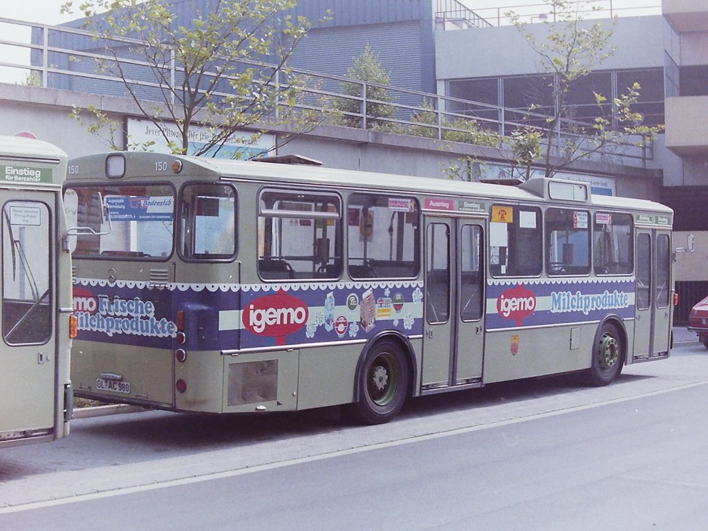 Wagen 150, OL-AC 980, EZ: 1975. Ein Jahrzehnt war Wagen 150 mit diesem Aussehen im Oldenburger Liniennetz unterwegs. Er war der einzige, der 16 angeschafften O 305, der sein Werbeband in dieser Form um das Heck herum trug. Der Bus war zudem der letzte Linienbus der Oldenburger Vorortbahnen Pekol, der im alten  Pekolgr�n  zugelassen wurde. Die Aufnahme entstand im August 1984 auf der Reserveposition am Bundesbahnweg. 