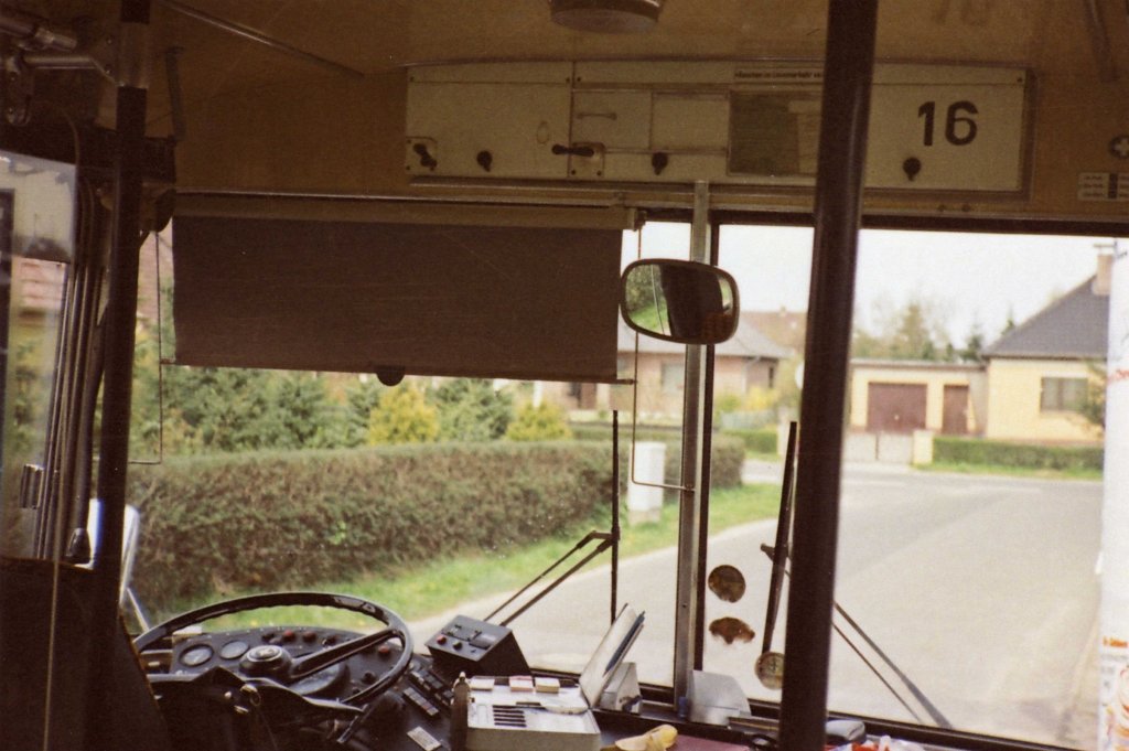 Wagen 16, .... nun ein Blick AUS dem Bus, der uns aber auch erlaubt mal den Arbeitsplatz im SETRA von einer anderen Perspektive aus zu betrachten. Direkt an der Front unter der Decke erkennt man den inneren Teil des Zielschildkasten. Die beiden Kurbeln waren f�r etwas kurz gewachsene Fahrer gar nicht so leicht zu erreichen. Um die Linienkennung beim Verstellen auch sehen zu k�nnen mussten die Fahrer eine kleine Klappe �ffnen. Zum Verstellen des Zielschildes reichte das Beiseiteschieben des kleinen mit einem Griff versehenen Bleches neben der Kurbel aus. Hinter einer Kunststofffolie daneben steckten die ben�tigten Zulassungen des Busses. Der obligatorische Zahltisch enthielt die Wechselvorrichtung f�r M�nzgeld, eine Schublade f�r Geldscheine, in die auch die  Heierm�nner  flogen, so nannte man die alten 5,-DM M�nzen, die Halterung f�r den Stempel, die Fahrscheinbl�cke und schlie�lich den Kursplan mit den wichtigsten Abfahrts- und Durchlaufzeiten. Die sogenannte  �TV-Banane  befindet sich �brigens auf dem Bild links vom Zahltisch. So wurde das Amaturenbrett der V�V-Busse in Anspielung auf seine Form und den Namen der gewerkschaftlichen Vertretung der meisten Angeh�rigen im �ffentlichen Dienst (�ffentliche Dienste, Transport und Verkehr) genannt. Daran befindet sich auch der Steuerungskasten f�r die automatischen Fahrscheinentwerter. Mit dem roten Knopf konnte diese gesperrt werden, um Schwarzfahrern die M�glichkeit zu nehmen, bei Erkennen eines Kontrolleurs ihren Fahrschein noch zu entwerten. Mit diesem Bild enden die Beitr�ge von Werner Striepling zu diesen Seiten. Sein eigentliches Interesse in der damaligen Zeit galt vor allem den Bussen der Deutschen Bahn und der Deutschen Post. Viele Bilder, die er hier zur Verf�gung gestellt hat, entstanden eher zuf�llig, weil sich gerade mal die Gelegenheit bot oder ein Film vollgemacht werden sollte um die Entwicklung zu erm�glichen. So war das damals, als es noch keine digitale Fotografie gab. Ich m�chte mich denn auch an dieser Stelle nochmals aufrichtig und ganz herzlich f�r die zugesandten Bilder und die vielen wertvollen Informationen bedanken, die die bislang gezeigten Bilder und Beitr�ge unterst�tzt und erg�nzt haben. Ich bin �berzeugt, dass die Besucher dieser Seiten diese Einsch�tzung teilen. Vielen, vielen Dank !