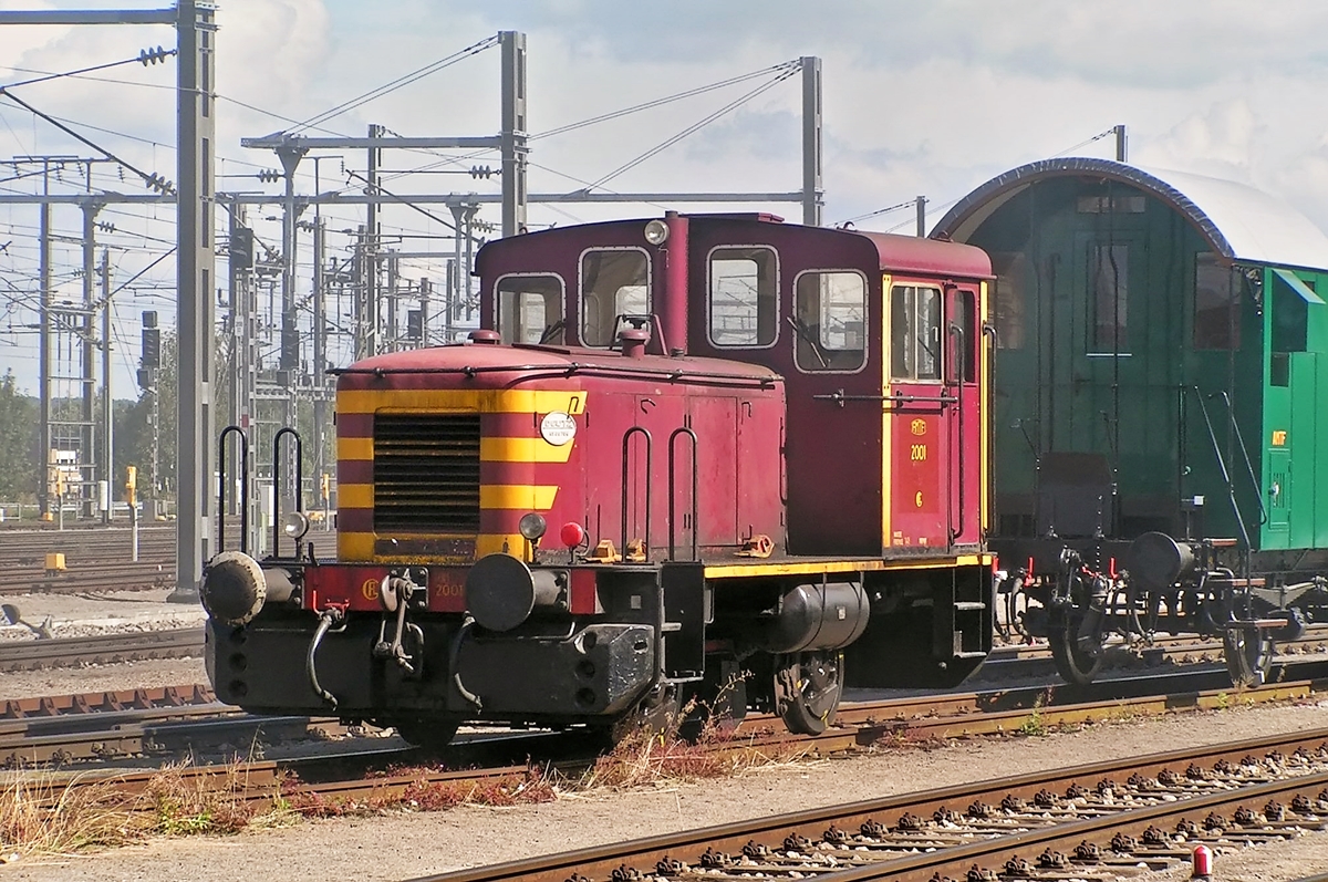 . Am 19.09.2004 rangierte die ex CFL 2001 die Museumsbahnwagen im verrauchten Bahnhof von P�tange. (Hans)

Diese Lok ist ein Kuriosum und kann deshalb in keine der Kategorien f�r luxemburgische Dieselloks einsortiert werden.

Die 2001 ist eine Deutz Lok vom Typ A 12 L 614. �usserlich �hnelt sie den Loks der S�rie 1020, aber w�hrend diese �ber ein Nachschaltgetriebe durch Triplex-Rollenketten angetrieben werden, erfolgt dies bei der 2001 �ber Kuppelstangen und einer zwischen den Achsen angeordneten Blindwelle.

Unter der Nummer 2001 kam sie vorerst als Werkslok zum Betriebswerk Luxemburg. Warum die aus dem Rahmen fallende Nummer 2001 gew�hlt wurde, ist nicht �berliefert. Normal w�re de Nummer 1031 gewesen.

Nachdem die Lok 1988 bei der CFL ausgemustert wurde, kam sie im Fr�hjahr 2001 zur Museumsbahn Train 1900 nach Fond de Gras.

Die technischen Daten der 2001:

Baujahr: 1957
Baunummer: 56764
Spurweite: 1435 mm
Dienstgewicht: 28 t
Leergewicht: 27 t
Achsdruck: 14 t
Achsstand: 2650 mm
Laufkreisdurchmesser der R�der: 850 mm
Kleinst befahrbarer Kurvenradius: 60 m

