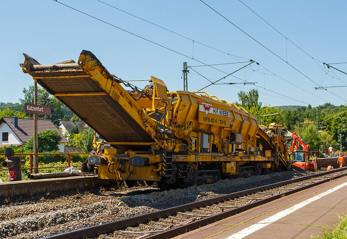 Baustelle im Bahnhof Katzenfurt (Lahn-Dill-Kreis) am 20.07.2013: Der MFS 40/4-B-ZW (mit Bagger) der H. F. Wiebe, Schweres Nebenfahrzeug 90 80 9052 001-1 D-GBM (ex 97 19 13 501 57-5) ist im Einsatz, der integrierte Bagger ist beim Aushub des Oberbaumaterials (Schotter und Planum).

Der MFS 40/4-B-ZW wurden 2009 von Plasser & Theurer unter der Fabriknummer 5479 gebaut und an die Wiebe Gleisbaumaschinen GmbH (Achim) geliefert.

Die MSF-ZW können sich durch seine beiden selbstständig angetriebenen Raupenfahrwerke im gleislosen Baustellenbereich fortbewegen, bzw. durch seine beiden Laufdrehgestelle, vorausgesetzt er besitzt vor sich einen MFS oder einen Schutzwagen mit Auflagerbock für vorragendes Schwenkband, in Züge eingestellt werde

Die beiden MFS 40/4-ZW sind für den gleislosen Einsatz konzipiert. Der MFS 40/4-ZW-B ist, im Bereich des Beladebandes, mit einem Bagger ausgerüstet, mit dessen Hilfe das vorhandene Planum/Aushub aufgenommen und über das Förderband in den Bunker befördert und gespeichert wird. Ist der Bunker fast voll, fährt der ebenfalls mit Raupenfahrwerken ausgestatteten MFS 40/4-ZW-A heran und der Aushub wird an ihn übergeben. Der MFS 40/4-ZW-B kann kontinuierlich weiter arbeiten, während nun der MFS 40/4-ZW-A, in der Zwischenzeit das Material auf im Gleis stehende gleisgebundene MFS, bringt und an diese übergibt. Die MFS sind mit einer eigenen Energieversorgungseinheit ausgestattet, wodurch ein individueller, also voneinander unabhängiger, Einsatz gewährleistet ist.  

TECHNISCHE DATEN des MFS 40/4-ZW-B:
Hersteller: Plasser & Theurer, Fabriknummer 5479 (2009)
Spurweite: 1.435 mm (Normalspur) / oder auf Raupenfahrwerke
Gesamtlänge: 23.920 mm (über alles) 
Länge über Puffer: 19.900 mm
Drehzapfenabstand: 13.000 mm
Breite: 3.150 mm
Höhe: 4.600 mm
Eigengewicht: 72.800 kg
Gesamtgewicht auf Drehgestell: 72.800 kg (leer)
Gesamtgewicht auf Raupe beladen: 128 t
Eigenfahrgeschwindigkeit auf Raupen: bis 3 km/h
Max. Siloinhalt: 25 m³
Förderleistung: 500 m³/h
Kleinster befahrbarer Gleisbogen: R 150 m
Dieselmotor: wassergekühlter 6-Zylinder Reihenmotoren mit Common-Rail-Einspritzsystem, Turboaufladung und Ladeluftkühlung, vom Typ Deutz TCD 2013 L06 2V mit einer Leistung von 160 kW  
Höchstgeschwindigkeit im Zugverband: 100 km/h (geschleppt)

