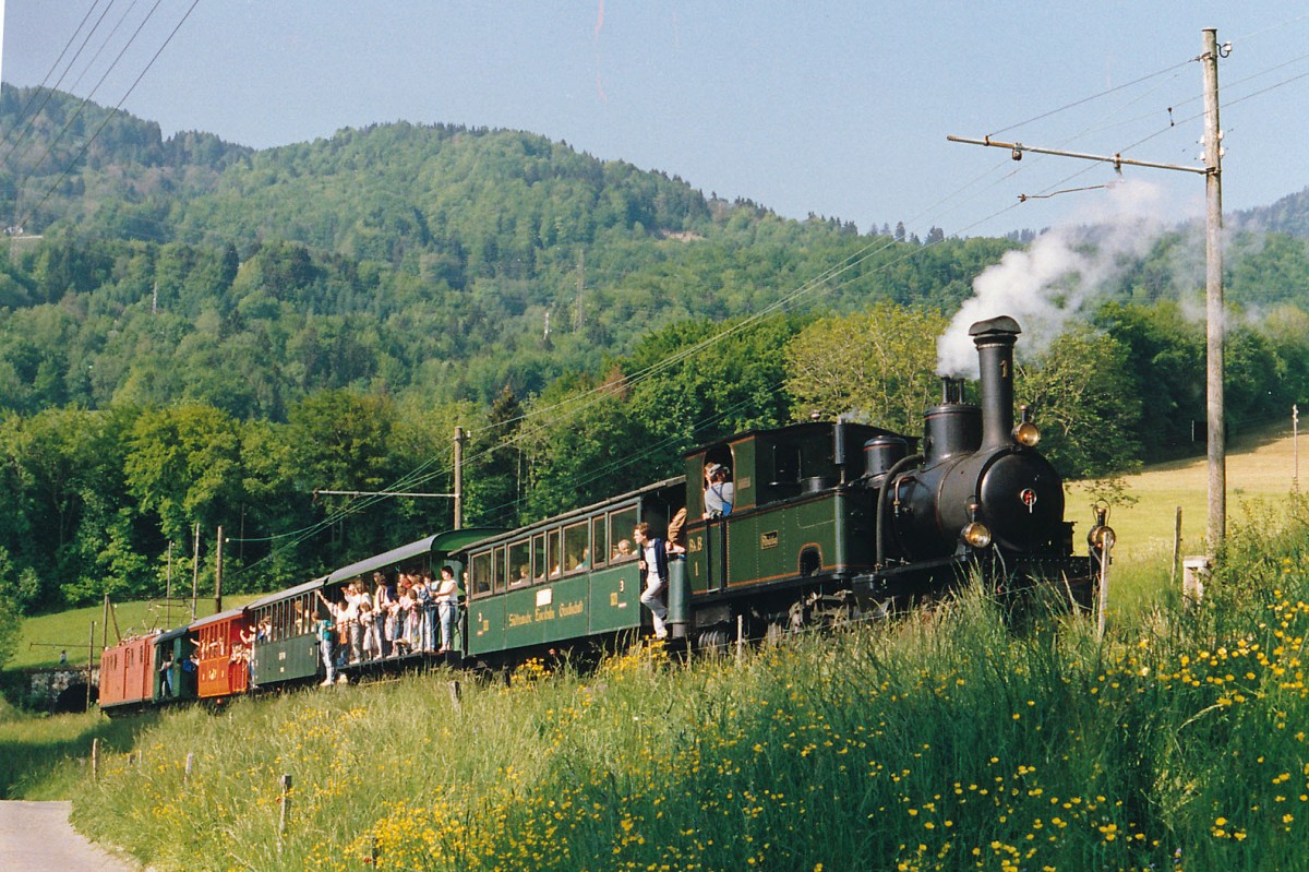 BC: Dampf-Festival auf der Blonay-Chamby-Bahn während dem Pfingstwochenende 1986. Was sich seit dem Jahre 1986 verändert hat: Der Bahnfotograf war damals noch mit der analogen Canon-Spiegelreflexkamera und lichtempfindlichen Kodak 100 ASA Filmen unterwegs. Auch wurde der lange Dampfsonderzug mit 5 Wagen damals noch mit zwei ehemaligen RhB-Lokomotiven geführt. Auf der Fahrt von Blonay nach Chamby leistete die Ge 4/4 181 (1916), ehemals RhB Bernina der G 3/4 1  Rhätia  (1889), ehemals RhB, Schiebedienst. Die Aufnahme entstand im Mai 1986 bei Cornaux. Die Rhätia stand seit dem Jahre 1970 bei der BC im Einsatz. Ab dem Jahre 1988 dampft sie nach einer aufwendigen Aufarbeitung wieder im Bündnerland auf ihren ehemaligen Stammstrecken.
Foto: Walter Ruetsch 