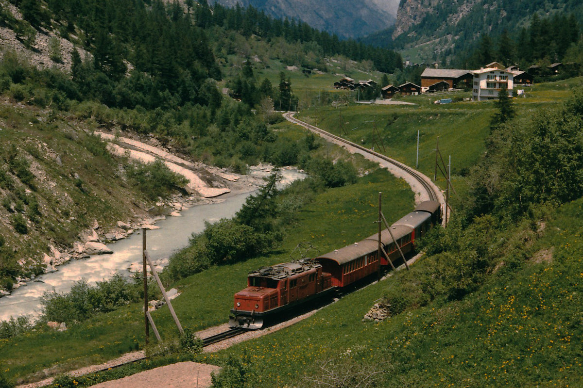 BVZ: Ein gemischter Zug mit der HGe 4/4 15 auf der Fahrt nach Zermatt im Juni 1986. Nebst zwei Wagen mit offenen Blattformen wurde noch ein Post- und G�terwagen mitgef�hrt. Zu dieser Zeit gab es auch noch die speziellen h�lzernen Fahrleitungsmasten.
Foto: Walter Ruetsch 