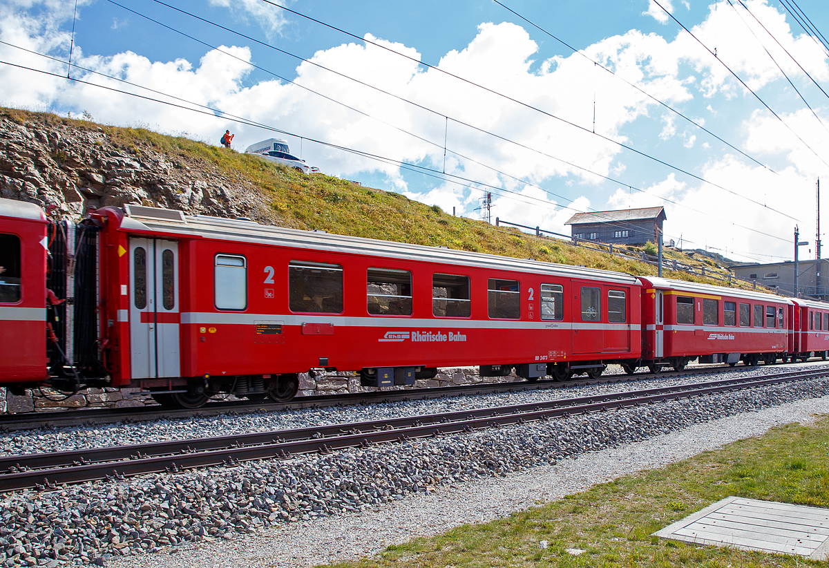 Der 4-achsige 2.Klasse Personenwagen mit Gep�ckabteil RhB BD 2473, ein verk�rzter Einheitswagen II (EW II bzw. FFA2) mit Aluminiumwagenkasten am 06.09.2021 bei der Station Ospizio Bernina im Zugverband.

Gestiegene Fahrgastzahlen und Komfortanspr�che veranlassten die RhB, das bew�hrte Konzept des Einheitswagen I nach etwa einem Jahrzehnt zu �berarbeiten und den sogenannten Einheitswagen II (EW II) mit der Industrie zu entwickeln. Mehr als 60 Fahrzeuge dieser Serie konnten �ber einen Zeitraum von acht Jahren beschafft werden. Hierzu z�hlen auch Sonderbauarten, wie die vier als BD 2471 - 2474 bezeichneten 2. Klasse Wagen mit Gep�ckabteil, die Steuerwagen BDt 1721 – 1723 und der Speisewagen WR 3815.

Als Verbesserung gegen�ber den EW I gelten neue Drehgestelle vom Typ SWP 74, der vergr��erte Sitzteiler (1.780 mm) in der 2. Klasse, get�nte Doppelverglasung und ein verbessertes Heizungs- und L�ftungssystem (�Hagenuk�). Trotz neuer Stoffbez�ge in der zweiten Wagenklasse, die Anfang der neunziger Jahre die roten und gr�nen Kunststoffsitzbez�ge abgel�st haben, wirkt das Interieur dieser Fahrzeuge heute gegen�ber den modernisierten EW I etwas altmodisch. Folgerichtig hat die RhB mit einem umfangreichen Refit-Programm begonnen. Neben einem modernen geschlossenen Toiletten-System erhalten diese Wagen, Dachklimager�te, ein neues Fahrgast-Informationssystem mit Innen- und Au�enanzeigen. Ferner wird die Inneneinrichtung zeitgem�� gestaltet.

TECHNISCHE DATEN:
Baujahre: 1975 bis 1984 (dieser 1982)
Hersteller:  Flug- und Fahrzeugwerke Altenrhein AG (FFA)
Hersteller Drehgestelle: Schindler Waggon Pratteln (SWP) 
Spurweite: 1.000 mm
Anzahl der Achsen: 4
L�nge �ber Puffer: 16.450 mm
Drehgestellbauart: SWP 74
Sitzpl�tze: 27 (2.Klasse)
Eigengewicht: 14,0 t
Ladegewicht: 3,5 t
zul�ssige Geschwindigkeit: 90 km/h
Lauff�hig: StN (Stammnetz) / BB (Berniabahn) / MGB (Matterhorn Gotthard Bahn)
