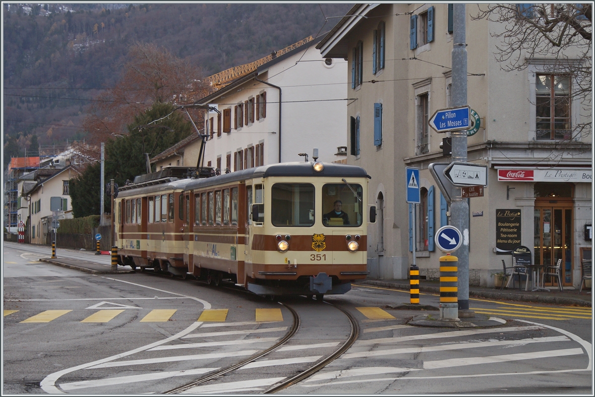 Der A-L Regionalzug 329 von Leysin nach Aigle bestehend aus dem Bt 351 und dem BDeh 4/4 302 haben den Halt Aigle-Place-du-March� verlassen und �berqueren nun eine Kreuzung um dann durch die Altstadt zum Bahnhof von Aigle zu kommen. 

5. Dezember 2021
