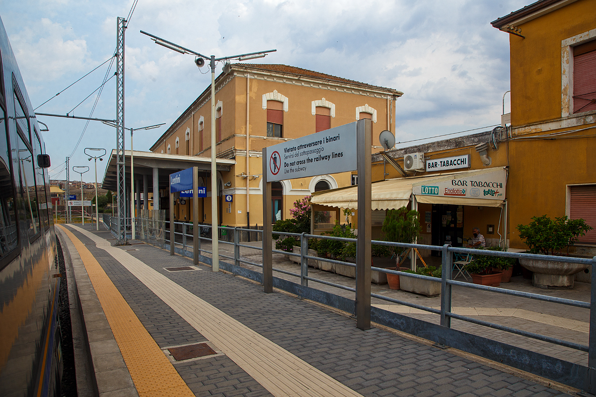 Der Bahnhof Lentini/Sizilien (italienisch Stazione di Lentini/Sicilia) bei km 154,4 an der Bahnstrecke Messina–Syrakus (RFI 152) am 19 Juli 2022.

Der Bahnhof Lentini wurde im Rahmen des Eisenbahnbauprojekts der Gesellschaft Vittorio Emanuele errichtet, welches von der Societ� per le strade ferrate della Sicilia (Sizilianischen Eisenbahngesellschaft) fortgef�hrt wurde. Er war Teil des Projekts, die Gegend um Syrakus (Siracusa) per Eisenbahn mit der Stadt und dem Hafen von Catania zu verbinden und landwirtschaftliche Produkte, insbesondere Zitrusfr�chte, aus der Gegend um Lentini und der Ebene von Catania zu den M�rkten zu transportieren. Der Bahnhof wurde am n�rdlichen Stadtrand von Lentini, in der N�he des Lentini-Sees, errichtet und am 1. Juli 1869 eingeweiht, zeitgleich mit der Er�ffnung der Eisenbahnlinie Catania Centrale nach Lentini. Am 19. Januar 1871 wurde er mit der Er�ffnung des letzten 57,8 km langen Abschnitts bis zum Bahnhof Syrakus (Siracusa) auch mit Syrakus, im S�dosten von Sizilien, verbunden.

Neben den Regionalz�ge halten in dem Bahnhof auch Fernverkehrsz�ge der Gattung Intercity (IC) und Intercity Notte (ICN). 

Ca. 4 km n�rdlich in Lentini Diramazione zweigt zudem die Bahnstrecke (RFI 154) nach Gela ab.

Merkmale
Der Bahnhof besteht aus einem zweist�ckigen Geb�ude am s�dlichen Ende des Gleiskomplexes. Das Bahnhofsgeb�ude befindet sich westlich der Gleise. Der Bahnhof ist ein Haltepunkt f�r Personenz�ge aller Kategorien.

Der Gleiskomplex umfasst das erste Durchgangsgleis, ein �berholgleis und ein Vorranggleis f�r den Personenverkehr sowie mehrere G�tergleise. Nur das erste Gleis verf�gt �ber einen Unterstand. Die verschiedenen G�ter- und Abstellgleise befinden sich auf der Westseite des Bahnhofs. Fr�her fuhren viele G�terz�ge mit Zitrusfr�chten vom Bahnhof Lentini ab. Seit Ende der 1980er Jahre ist der Verkehr deutlich zur�ckgegangen.

Am 15. Dezember 2019 weihte der Pr�sident der Region Sizilien den modernisierten Bahnhof ein. Insbesondere wurde eine Unterf�hrung mit Rampen f�r Behinderte und neue Bahnsteige errichtet. 

Quellen: Wikipedia (Italien) 
Stand: September 2025
