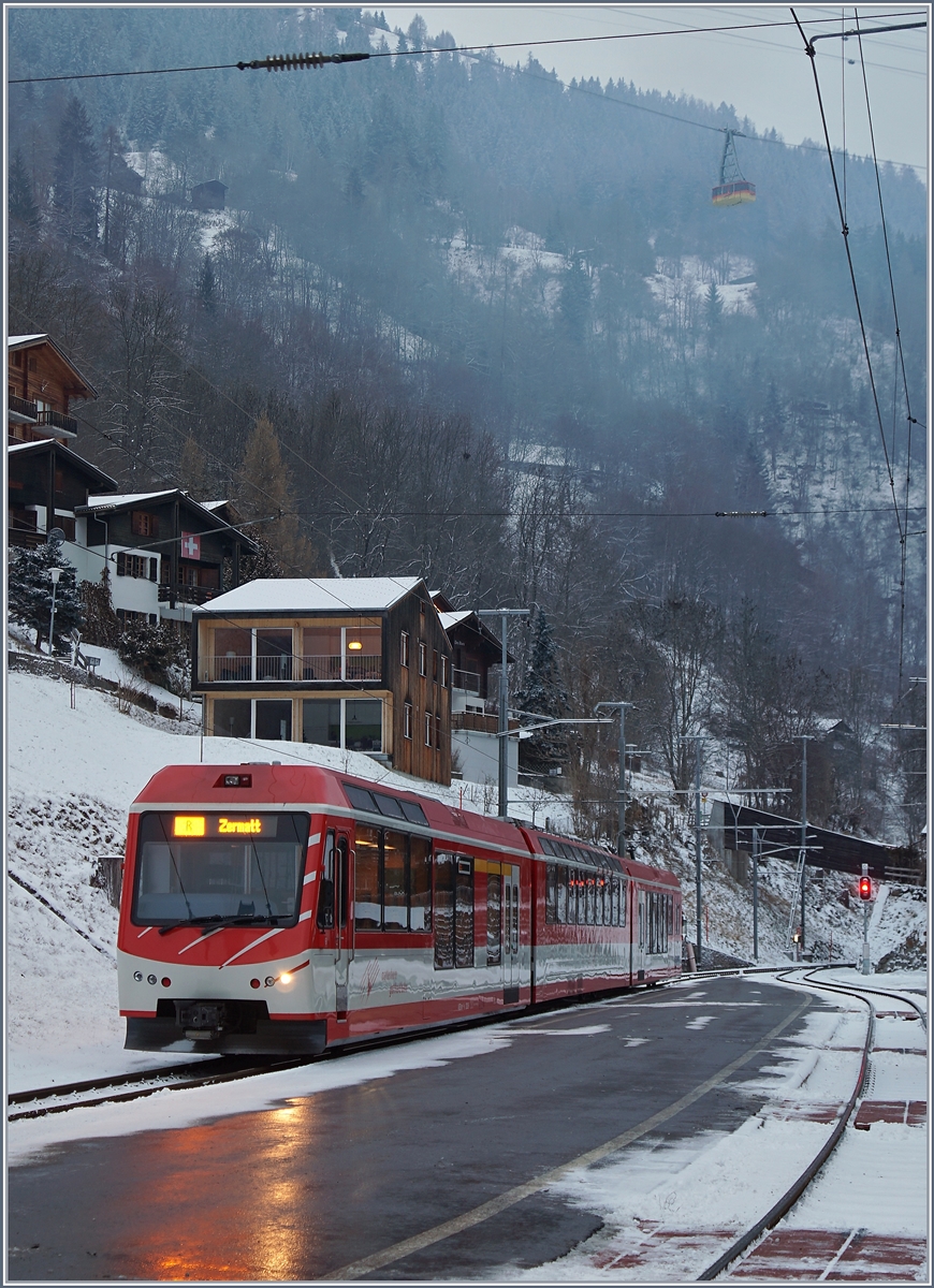Der MGB ABDeh 4/8 2026 wartet in seinem Zugsausgangsbahnhof Fiesch auf die Abfahrt nach Zermatt, w�hrend im Hintergrund, schlecht sichtbar, eine Seilbahn aus Eggishorn schwebt.
5. Jan. 2017