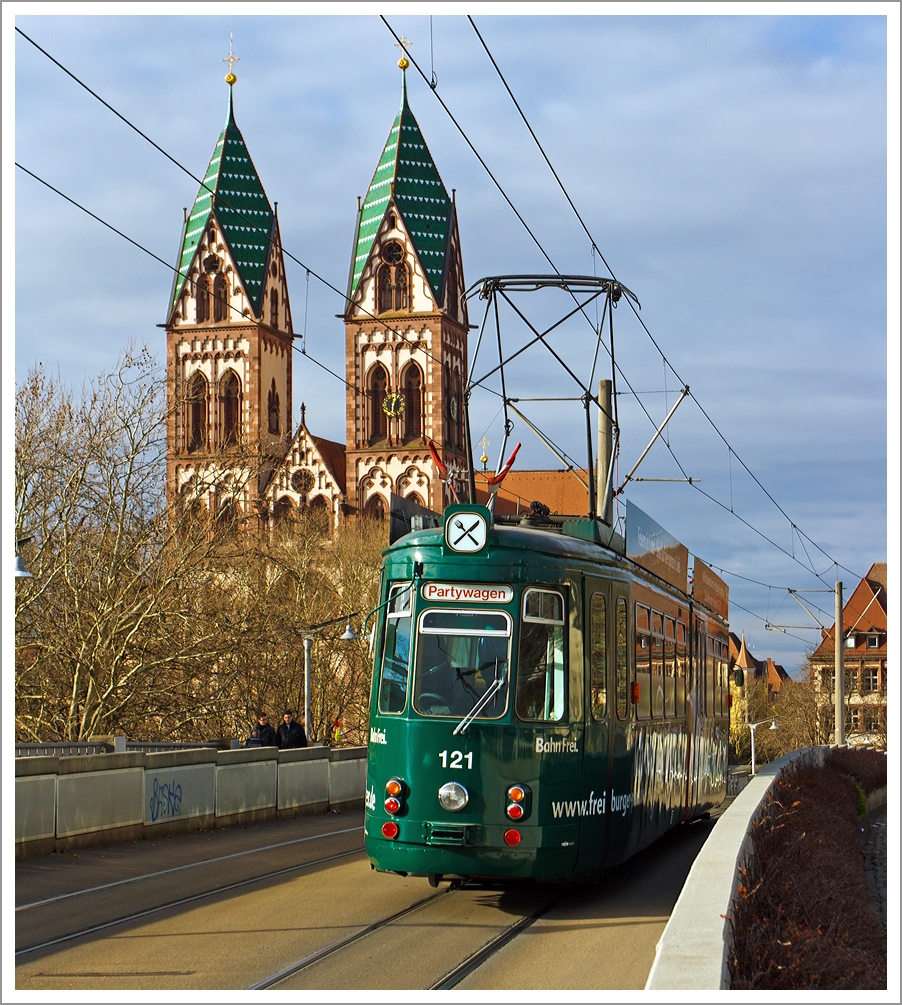 Der Partywagen 121 der Freiburger Verkehrs AG (VAG) überquert die Stühlingerbrücke (Freiburg im Breisgau) am 07.12.2013, im Hintergund die Herz-Jesu-Kirche.

Der Wagen ist ein GT4 (vierachsige Straßenbahn-Kurzgelenktriebwagen in Zweirichtungsausführung) und wurde 1968 von der Waggonfabrik Rastatt gebaut, 1995 erfolgte der Umbau zum Partywagen. 

Technische Daten: 
Achsformel:  (1A)(A1)
Spurweite:  1.000 mm (Meterspur)
Länge über Kupplung:  17.430 mm
Breite:  2.200 mm
Leergewicht:  19.000 kg
Höchstgeschwindigkeit:  50 km/h
Stundenleistung:  2 × 100 kW = 200 kW
Stromsystem:  600 Volt Gleichstrom

Zwischen 1962 und 1968 beschaffte die Freiburger Verkehrs AG 19 dieser GT 4 nach Vorbild von der Stuttgarter Straßenbahnen entwickelten Kurzgelenktriebwagen des Typs SSB GT4 in Zweirichtungsversion, mit einigen Änderungen. Bei der Maschinenfabrik Esslingen wurden 11 Wagen gebaut (1962 und 1966) und 8 weitere wurden 1967 und 1998 aber von der Waggonfabrik Rastatt gebaut, weil die Maschinenfabrik Esslingen keine Straßenbahnen mehr herstellte. 

