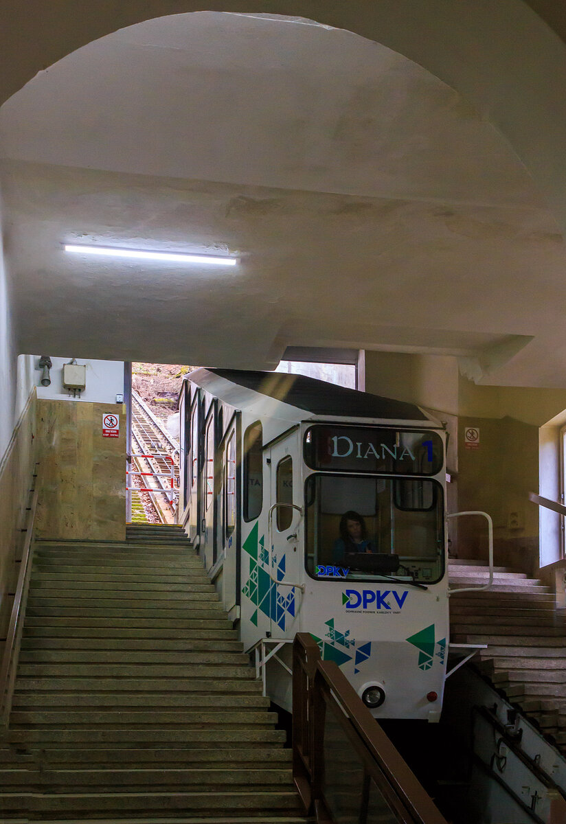 Der Wagen „DIANA 1“ der Standseilbahn Diana (tschechisch Lanová dráha Diana) in Karlsbad (Karlovy Vary) erreicht am 18.04.2023 die Talstation Stará louka (Alte Wiese).

Die Stadtseilbahnen (Diana sowie Imperial) stellen in Karlsbad schon seit Anfang des vergangenen Jahrhunderts ein traditionelles und beliebtes Verkehrsmittel dar. Sie gehören inzwischen zum Stadtbild und sind ein beliebtes Touristenziel.

Diana-Standseilbahn:
Die Standseilbahn Diana (tschechisch Lanová dráha Diana) wurde im August 1912 eröffnet und beginnt an der Station Alte Wiese (Stará louka) auf einer Höhe von 389 m und führt auf die Freundschaftshöhe 556 m über NN, wo sich der Diana-Aussichtsturm befindet. Die Talstation befindet sich gleich neben dem Grandhotel Pupp in der Gasse Mariánská. Den Höhenunterschied von 167 m überwindet sie auf einer Strecke von 437 m. Im Bereich der abtsche Ausweiche liegt auch die Mittelstation Jelení skok (Hirschsprung) in 473 m Höhe. Die maximale Steigung beträgt 432,3 ‰, durchschnittlich liegt diese bei 398,1 ‰. Die Bahn wurde insgesamt dreimal renoviert, zwischen 1963 und 1965, 1972 und noch einmal zwischen 1984 und 1988. Im Gegensatz zur Bahn zum Personennahverkehrs der Stadt. Auch sie wird im 15-Minuten-Takt befahren und benötigt 4 Minuten für eine Fahrt bei einer Geschwindigkeit von 2,04 m/s. Die Gleise sind vom Typ A, die Spurweite beträgt 1.000 mm. Die leer 7.900 kg wiegenden Wagen sind für 49 + 1 Fahrer ausgelegt. Das Seil hat einen Durchmesser von 28 mm. Die Antriebsleistung beträgt 51 kW, die Antriebsregulation erfolgt mit Hilfe von Thyristoren, 

Die Seilbahn ist ein Projekt des Ing. H. H. Peter aus Zürich. Der Bau der Seilbahn wurde von der Wiener Baufirma Leo Arnoldi mit Hilfe von lokalen Handwerkern und Firmen durchgeführt. Die erste Generalüberholung der Seilbahn geschah in den Jahren 1963-1965, als die Seilbahnen neue Metallwagons aus der Produktion des Tatra Smíchov Wagon bekamen. Die Rekonstruktion der elektrischen Ausrüstung wurde 1972-73 durchgeführt.Es ist ein traditionelles und sehr beliebtes Verkehrsmittel auf der Freundschaftshöhe in Karlsbad, das hauptsächlich von den Touristen der Stadt genutzt wird. Von der Talstation wird man zum Gipfel gebracht, wo sich der Aussichtsturm Diana und das Wald-Restaurant und Café Diana befindet.

Betreiber der Seilbahnen ist die DPKV - Dopravní podnik Karlovy Vary a. s. (Verkehrsbetrieb Karlsbad AG). Der Verkehrsbetrieb Karlsbad AG ist ein traditioneller Betreiber des öffentlichen Verkehrs in Karlsbad. Er betreibt tagsüber und auch in den Nachtstunden die regelmäßigen Stadtbusverkehrslinien, Sonderverkehrslinien und Vorortverkehrslinien. Ein Besonderheit des Karlsbader ÖÖV ist der Verkehr der Stadtseilbahn vom Theaterplatz (Divadelní náměstí) zum Hotel Imperial und vom Grandhotel Pupp zum Aussichtsturm Diana. Der Verkehrsbetrieb Karlsbad AG bietet der Öffentlichkeit auch weitere, überwiegend mit der Beförderung zusammenhängende Dienstleistungen an. 

DATEN der Seilbahn DIANA:
Höhenunterschied: 167 m
Streckenlänge:  453 m
Spurweite: 1000 mm (Meterspur)
Maximale Steigung:  432,3 ‰
Leergewicht eines Wagens: 7.900 kg
Kapazität eines Wagens: 49 + 1 Fahrer
Seildurchmesser: 28 mm
Antriebsleistung: 51 kW
Höchstgeschwindigkeit: 7,3 km/h
Taktung: alle 15 Minuten
Fahrtdauer: ca. 3 Minuten
Preis (z.Z.) für Hin- und Rückfahrt: 150 CZK