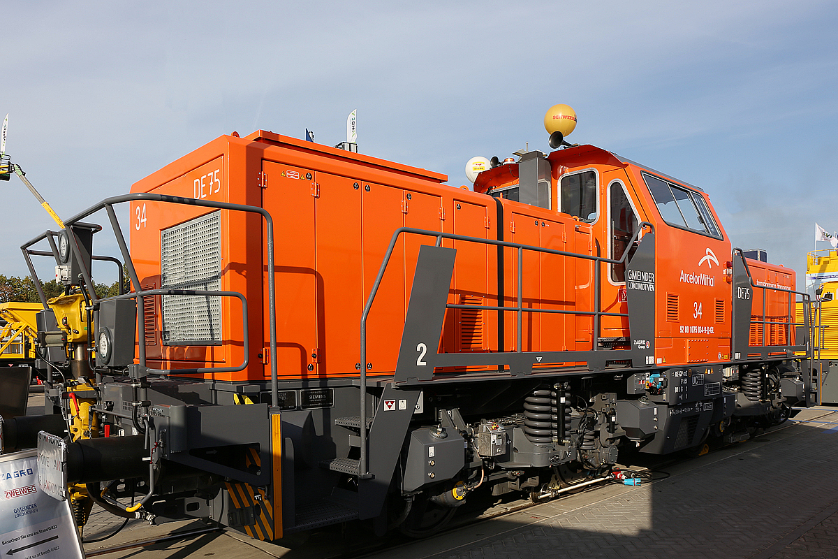 Der zur ZAGRO Group geh�rende Hersteller  GMEINDER LOKOMOTIVEN GmbH (Mosbach) pr�sentierte auf der InnoTrans 2018 in Berlin (hier 18.09.2018) seine Rangierlokomotive mit elektrischer Leistungs�bertragung DE75 BB Dual Engine, hier in Form der ArcelorMittal 34, NVR-Nummer 92 80 1075 034-9 D-GL.

Die DE 75 BB Dual Engine wurde 2018 von Gmeinder in Mosbach unter der Fabriknummer 5777 gebaut und hier auf der Messe  InnoTrans 2018  ausgestellt bevor sie dann an die ArcelorMittal Eisenh�ttenstadt Transport GmbH in Eisenh�ttenstadt als Lok 34 ArcelorMittal 1075 034-9 ausgeliefert wurde.

Die DE75 BB ist eine robuste Rangierlokomotive f�r den schweren Rangierdienst. Die elektrische Leistungs�bertragung mit vier unabh�ngig geregelten Fahrmotoren erm�glicht die optimale Ausnutzung der Adh�sion und gleichzeitig die Verwendung verschiedenster Energiequellen. Durch den symmetrischen Aufbau der Lokomotive k�nnen zwei Energiequellen eingebaut werden, zum Beispiel (wie hier) zwei Diesel-Generator-Aggregate (Dual-Engine Lokomotive) oder ein Dieselaggregat und ein Lithium-Ionen-Batteriesatz (Hybridlokomotive). Auch eine Energiezuf�hrung �ber Stromschiene (DC 750 V) oder Fahrdraht ist m�glich. Der symmetrische Aufbau der Lokomotive setzt sich auch in der Leistungselektronik fort. Zwei unabh�ngige Teilsysteme gew�hrleisten h�chste Verf�gbarkeit der Lokomotive.

Die ist zugelassen, Zugfahrten au�erhalb von Bahnh�fen sind jedoch nicht m�glich, da der Erstkunde Arcelor Mittal die Lok ohne Zugsicherung und Zugfunk geordert hat. 

TECHNISCHE DATEN der DE75 BB Dual Engine:
Hersteller:	GMEINDER LOKOMOTIVEN GmbH (Mosbach)
Spurweite:  1.435 mm
Achsformel: Bo‘ Bo‘
L�nge �ber Puffer: 14.080 mm
Drehzapfenabstand: 5.600 mm
Achsabstand im Drehgestell: 2.400 mm
Breite: 3.080 mm
H�he: 4.260 mm
Dienstgewicht: 80 t
Achslast: 20 t
H�chstgeschwindigkeit: 100 km/h
Min. Dauerfahrgeschwindigkeit: kleiner 1,0 km/h
Motorleistung: 2 x 354 kW
Leistung am Rad: 600 kW 
Anfahrzugkraft: 260 kN
Kleinster befahrbarer Gleisbogen: R  60 m
Tankinhalt: 1.900 Liter
Sandvorrat: 500 kg
Fahrzeugbegrenzung:   UIC 505-1
