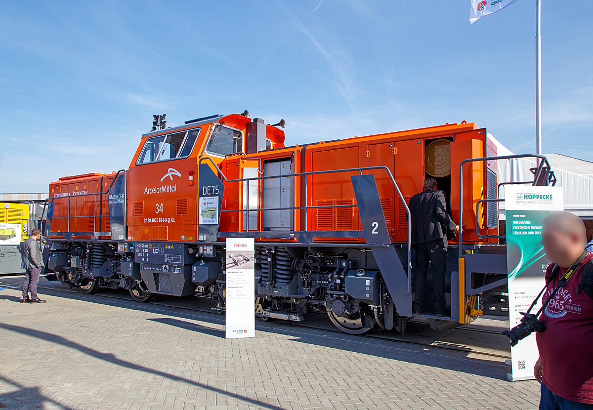 Der zur ZAGRO Group geh�rende Hersteller  GMEINDER LOKOMOTIVEN GmbH (Mosbach) pr�sentierte auf der InnoTrans 2018 in Berlin (hier 18.09.2018) seine Rangierlokomotive mit elektrischer Leistungs�bertragung DE75 BB Dual Engine, hier in Form der ArcelorMittal 34, NVR-Nummer 92 80 1075 034-9 D-GL.

Die DE 75 BB Dual Engine wurde 2018 von Gmeinder in Mosbach unter der Fabriknummer 5777 gebaut und hier auf der Messe  InnoTrans 2018  ausgestellt bevor sie dann an die ArcelorMittal Eisenh�ttenstadt Transport GmbH in Eisenh�ttenstadt als Lok 34 ArcelorMittal 1075 034-9 ausgeliefert wurde.

Die DE75 BB ist eine robuste Rangierlokomotive f�r den schweren Rangierdienst. Die elektrische Leistungs�bertragung mit vier unabh�ngig geregelten Fahrmotoren erm�glicht die optimale Ausnutzung der Adh�sion und gleichzeitig die Verwendung verschiedenster Energiequellen. Durch den symmetrischen Aufbau der Lokomotive k�nnen zwei Energiequellen eingebaut werden, zum Beispiel (wie hier) zwei Diesel-Generator-Aggregate (Dual-Engine Lokomotive) oder ein Dieselaggregat und ein Lithium-Ionen-Batteriesatz (Hybridlokomotive). Auch eine Energiezuf�hrung �ber Stromschiene (DC 750 V) oder Fahrdraht ist m�glich. Der symmetrische Aufbau der Lokomotive setzt sich auch in der Leistungselektronik fort. Zwei unabh�ngige Teilsysteme gew�hrleisten h�chste Verf�gbarkeit der Lokomotive.

Die ist zugelassen, Zugfahrten au�erhalb von Bahnh�fen sind jedoch nicht m�glich, da der Erstkunde Arcelor Mittal die Lok ohne Zugsicherung und Zugfunk geordert hat. 

TECHNISCHE DATEN der DE75 BB Dual Engine:
Hersteller:	GMEINDER LOKOMOTIVEN GmbH (Mosbach)
Spurweite:  1.435 mm
Achsformel: Bo‘ Bo‘
L�nge �ber Puffer: 14.080 mm
Drehzapfenabstand: 5.600 mm
Achsabstand im Drehgestell: 2.400 mm
Breite: 3.080 mm
H�he: 4.260 mm
Dienstgewicht: 80 t
Achslast: 20 t
H�chstgeschwindigkeit: 100 km/h
Min. Dauerfahrgeschwindigkeit: kleiner 1,0 km/h
Motorleistung: 2 x 354 kW
Leistung am Rad: 600 kW 
Anfahrzugkraft: 260 kN
Kleinster befahrbarer Gleisbogen: R  60 m
Tankinhalt: 1.900 Liter
Sandvorrat: 500 kg
Fahrzeugbegrenzung:   UIC 505-1
