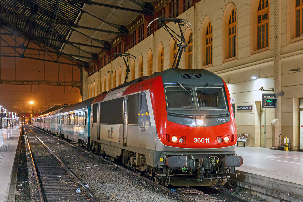 
Die Akiem 36011 (91 87 0036 011-1 F-AKIEM), eine Alstom BB 36000  Astride  (Asynchron Tricurrent Drive Engine), ist am 24.03.2015 gerade (um 22:29 Uhr) mit dem Thello EC 159 / EC 160 (Mailand - Genua  - Monte-Carlo - Niza - Toulon - Marseille-St-Charles) in den Endbahnhof Marseille St-Charles eingefahren.

Die BB 36000 ist eine Baureihe von elektrischen Lokomotiven der SNCF, mit dem Kosename  Astride  (Asynchron Tricurrent Drive Engine). Gebaut von Alstom (ehem. GEC-Alsthom), reihen sie sich ein in die Kategorie der europäischen asynchronen Mehrsystem-Lokomotiven. Mit ihren  großen  Schwestern, den BB 26000  Sybic  zählen sie zu den stärksten Lokomotiven der SNCF.

Die Astride besitzen drei unterschiedliche Stromabnehmer (1,5 kV Gleichstrom, 3 kV Gleichstrom und 25 kV 50 hz Wechselstrom). Diese Loks können in Belgien, in Luxemburg, in Italien, in Frankreich und neuerdings sogar in den Niederlanden verkehren. So sollte ein Lokwechsel an den Grenzen vermieden und eine Menge Zeit eingespart werden.

Nach der Bestellung von 264 Lokomotiven der Baureihe BB 26000  Sybic  entschied sich die SNCF für einen Kontraktwechsel. Daher bekamen die letzten 30 Neubau-Lokomotiven eine Drehstromausrüstung mit Asynchron-Motoren. Doch niemand zeigte Interesse an den neuen Loks. Genau zum selben Zeitpunkt wurden nämlich der Personenverkehr vom Güterverkehr bei der SNCF getrennt. Für den Personenverkehr wurde der TGV in den Focus gestellt und die meisten internationalen Nachtzüge abgeschafft. Der Güterverkehr zeigte auch kein Interesse an dieser polyvalenten Lok. Ebenfalls zu diesem Zeitpunkt, begann Alstom mit der Entwicklung der Prima, von der sie sich höhere Renditen erhoffte, sowohl in Frankreich, als auch im Ausland. Unter diesen Umständen war es schwer für die „Astride“ sich durchzusetzen, zu allem Übel litt sie auch noch lange unter verschiedenen Kinderkrankheiten.

Die insgesamt 60 gebauten BB 36000 „Astride“ wurden zwischen 1996 und 2002 ausgeliefert. Sie können eine gewisse Familienzugehörigkeit mit den BB 26000 nicht verleugnen, auch wenn die Ecken etwas abgerundet wurden und sie aerodynamischer ist, als die Sybic.

Obwohl sie Personenzüge mit 200, ja sogar 220 km/h ziehen kann, so wurde die „Astride“ doch vorwiegend im Güterverkehr zwischen Belgien und Italien eingesetzt. Dort ist ihre Geschwindigkeit allerdings auf 120 km/h begrenzt.

Im Oktober 2011 kamen die Loks mit den Nummern BB 36001,2,4,5,7,11 und 15 zu Akiem. Sie behielten zwar ihre  livrée multiservice , haben aber das SNCF Logo verloren. Drei von diesen Loks (BB36007, BB36011, BB36015) wurden bis 200 km/h getestet und fahren jetzt im internationalen Personenverkehr zwischen Paris und Venedig, sowie Marseille und Mailand. Diese Verbindungen werden von Thello, einer Tochtergesellschaft von Veolia betrieben.

Technische Daten der Baureihe BB 36000  Astride :
Betriebsnummern : 36001-36030, die 36331-36360 Italien tauglich, Mehrfachtraktion
Hersteller: GEC-Alsthom
Spurweite: 1.435 mm
Bauart: Bo'Bo'
Stromsystem: 1.500 V DC; 3.000 V DC und 25 kV, 50 Hz AC
Baujahre: 1996-2002

Länge über Puffer: 19.110 mm
Achsabstand im Drehgestell: 3.000 mm
Drehzapfenabstand: 10.400 mm
Breite: 2.926 mm
Höhe: 4.270 mm
Dienstgewicht: 89 t
Triebraddurchmesser (neu): 1.150 mm
Höchstgeschwindigkeit: 200 km/h (wenige 220 km/h)
Dauerleistung: 5.600 kW
Anfahrzugkraft: 320 kN
Anzahl der Fahrmotoren: 4 (4 FXA 4559 Alstom Asynchronmotoren mit Zwangsbelüftung)
