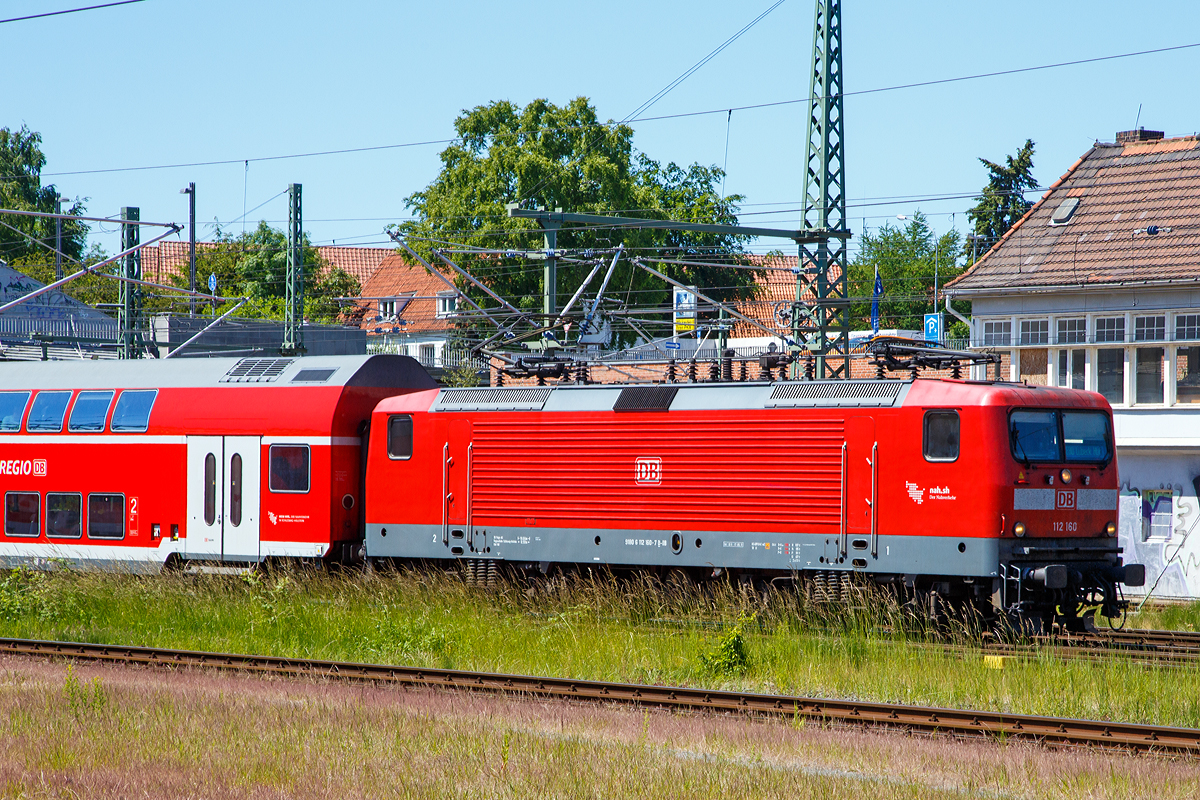 Die DB 112 160 (91 80 6112 160-7 D-DB) der DB Regio Nord erreicht am 11.06.2015 mit einem Regionalzug L�beck Hauptbahnhof.

Die Lok wurde von AEG in Hennigsdorf (zu DDR Zeiten LEW - VEB Lokomotivbau Elektrotechnische Werke „Hans Beimler“ Hennigsdorf) unter der Fabriknummer 21505 gebaut.

Die 112.1 wurde unverhofft zu einem Symbol f�r die Deutsche Einheit, denn sie war die erste Lokomotivbaureihe, die von beiden Bahnverwaltungen gemeinsam beschafft wurde. Man kam �berein, dass DR und DB jeweils 45 Loks der leicht verbesserten Loks der DR-Baureihe 112 bei der AEG bestellen w�rden (die AEG hatte zwischenzeitlich ihr 1946 enteignetes Werk in Hennigsdorf wieder �bernommen). Dies erfolgte haupts�chlich aus arbeitsmarktpolitischen Gr�nden zur St�tzung des Hennigsdorfer Werkes, denn die Bundesbahn h�tte lieber eine 200 km/h schnelle und universell verwendbare Lok in aktueller Drehstromtechnik nach Art der Baureihe 120 beschafft.

Die �u�erlich auff�lligste �nderung ist die Zusammenlegung der gro�en Spitzen- bzw. Schlusslichter zu kleinen kombinierten Halogenlampen, so wie es bei der alten DB seit jeher gang und g�be ist. 

Entwicklung:
Ab 1976 wurde von der Deutschen Reichsbahn in der DDR die Streckenelektrifizierung auf Grund der �lverteuerung wieder forciert, nachdem man zehn Jahre zuvor noch ganz auf Diesellokomotiven gesetzt hatte. Der VEB Lokomotivbau Elektrotechnische Werke „Hans Beimler“ Hennigsdorf (LEW), einziger Hersteller von Elloks in der DDR, bekam den Auftrag, ausgehend von der bew�hrten schweren G�terzuglok der Baureihe 250 eine leichtere und technisch modernere vierachsige Variante f�r den Personenzug- und mittelschweren G�terzugdienst zu entwickeln. Diese sollte ohne betriebliche Einschr�nkungen die Lokomotiven der Baureihe 211 im Schnellzug- und die der Baureihe 242 im G�terzugdienst ersetzen k�nnen. Die mechanischen Komponenten wurden in Hennigsdorf entwickelt und hergestellt. Die Fahrmotoren kamen vom VEB Sachsenwerk Dresden.

Auf der Leipziger Fr�hjahrsmesse 1982 wurde der Prototyp 212 001 der �ffentlichkeit vorgestellt. Die Lokomotive machte vor allem durch ihr attraktives �u�eres (wei� mit roten Streifen) von sich reden und bekam von den Besuchern den Spitznamen Wei�e Lady. Nach der Messe begann die DR mit der Erprobung der 140 km/h schnellen Lok, die konstruktiv f�r 160 km/h ausgelegt war. Nach der Probezerlegung im Ausbesserungswerk Dessau wurde die Getriebe�bersetzung ge�ndert und die Maschine am 14. Oktober 1983 in 243 001 umbezeichnet. Durch die ge�nderte �bersetzung konnte die Zugkraft deutlich erh�ht werden, wobei die zul�ssige Geschwindigkeit auf 120 km/h reduziert wurde.

Serienfertigung DR-Baureihe 243, sp�tere DB-Baureihe 143
Da zu diesem Zeitpunkt (1984) im DR-Netz kaum mehr als 120 km/h gefahren werden durfte, wurden zun�chst Mehrzwecklokomotiven der Reihe 243 beschafft. Von 1984 bis 1990 wurden 640 Loks gebaut.

Die DR-Baureihe 212, sp�tere DB-Baureihe 112.0
Da man bei der DR bis zuletzt davon ausgegangen war, dass der Ausbau der Transitstrecken nach West-Berlin und deren Elektrifizierung durch die Bundesrepublik finanziert w�rde, wurde erst 1991 mit dem Ausbau bestimmter Streckenabschnitte f�r mehr als 120 km/h begonnen. Allerdings standen bei der Deutschen Reichsbahn keine entsprechend schnellen Lokomotiven zur Verf�gung. Es mussten neue, schnelle Lokomotiven beschafft werden. Man erinnerte sich daran, dass der Prototyp 212 001(sp�ter 243 001) urspr�nglich f�r 160 km/h ausgelegt worden war. Nach vier Vorserienlokomotiven (212 002 bis 212 005) folgte eine Auslieferung von 35 Serienlokomotiven, bereits als 112 006 bis 040 bezeichnet. 

Von 1992 bis1994 wurden dann 90 verbesserte Loks (je 45 DR und DB) der Baureihe 112.1 von AEG gebaut. Ab Anfang 2001 standen diesie 90 Maschinen (der BR 112.1) aufgrund von Anrissen in der Aufh�ngung der Schlingerd�mpfer f�r den hochwertigen Reisezugdienst nicht zur Verf�gung. Die zul�ssige H�chstgeschwindigkeit wurde auf 140 km/h herabgesetzt und alle Schlingerd�mpfer untersucht. Dar�ber hinaus wurde die Pr�fung der D�mpfer im Rahmen der regelm��igen Instandhaltung vorgeschrieben. Ende Januar 2001 standen die ersten Maschinen wieder mit einer zul�ssigen Geschwindigkeit von 160 km/h zur Verf�gung.

Die 112.1 fand nach �berwindung einiger Kinderkrankheiten ihr Hauptbet�tigungsfeld in der neu geschaffenen Zuggattung Interregio, aber auch den einen oder anderen InterCity bespannte sie. Durch den Wegfall der Gattung IR und den Ausbau des RE-Netzes mit 140-km/h- und 160-km/h-f�higem Wagenmaterial sind die Lokomotiven heute vorwiegend im Regionalverkehr anzutreffen. Die DB Fernverkehr gab deshalb zum 1. Januar 2004 alle ihre 112.1 an die DB Regio ab. 

DB-Baureihe 114.0
Alle Lokomotiven der Baureihe 112.0 wurden 2000 in die Baureihe 114 umgezeichnet, weil sie fortan zum Bestand von DB Regio geh�rten, die Baureihe 112.1 verblieb ja noch beim Fernverkehr. Somit wollte man Verwechslungen zwischen den beiden Serien und damit auch zwischen Nah- und Fernverkehr vermeiden. Als die Fahrzeuge der Baureihe 112.1 auch in den Bestand von DB Regio eingereiht wurden, ist allerdings keine R�ckumzeichnung der Baureihe 114 vorgenommen worden. 

TECHNISCHE DATEN der BR 112.1:
Hersteller: 	AEG
Baujahre: 1992 bis 1994 
Ausmusterung: seit 2019
Spurweite: 1.435 mm (Normalspur)
Achsformel: Bo’Bo’
L�nge �ber Puffer: 16.640 mm
Drehzapfenabstand: 8.400 mm
Achsabstand im Drehgestell: 3.300 mm
H�he: 3.980 mm
Breite: 3.120 mm
Dienstgewicht: 82,5 t
H�chstgeschwindigkeit: 160 km/h
Stundenleistung: 4.220 kW
Dauerleistung:  4.000 kW
Anfahrzugkraft:  226 kN
Stromsystem: 15 kV, 16,7 Hz~
Anzahl der Fahrmotoren: 4
Antrieb: LEW-Kegelringfeder
Bremse: KE-Druckluftbremse; elektrische Widerstandsbremse, 2.200 kW Dauerleistung (kurzzeitig bis 2.690 kW belastbar)
Zugbeeinflussung: LZB I 80
