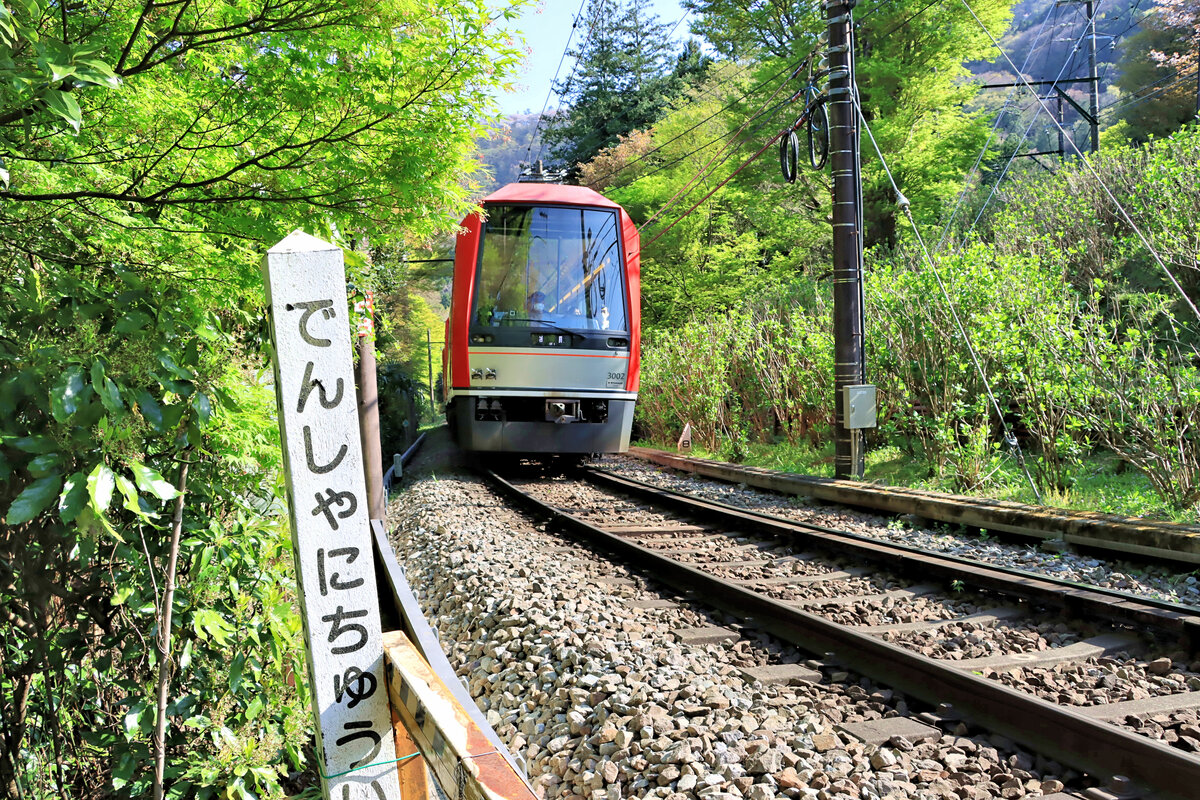 Die Hakone Tozan Bahn, Partnerbahn der RhB, im unteren Abschnitt: Ein neuer Panoramazug mit Triebwagen 3002 erklimmt die Steigung von der unteren zur mittleren Spitzkehre in Ôhiradai. Die Tafel besagt  Achtung auf den Zug . 12.April 2022 