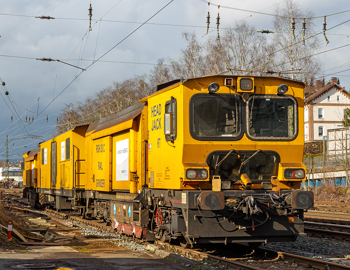 
Die Harsco Track Technologies Gleis- und Weichenschleifmaschine (engl. Rail Grinder) RGH 20 C  „Head Jack'“,  Schweres Nebenfahrzeug Nr. 97 32 97 50 117-1, der voestalpine BWG GmbH aus Butzbach (Betreiber – EVU: Hessische G�terbahn GmbH) ist am 04.03.2015 in Kreuztal abgestellt. 

Der Schienenschleifzug wurde 2003 von der Harsco Track Technologies (HTT) in den USA unter den Fabriknummern 257748 und 257749 gebaut. Der Fahrzeug hat die EBA-Nummer EBA 03C18A001.

Der Schienenschleifzug ist dreiteilig, an beiden Enden befinden sie die selbstfahrende 4-achsige (2 Drehgestelle) 10-Steine-Schienenschleifmaschinen (RGH 10C2-28) und dazwischen ein antriebsloser zweiachsiger Mittelwagen. Die selbstfahrende 20-Steine-Schienenschleifmaschine dient zur Beseitigung von Fahrfl�chenfehlern, Sch�den aus Rollkontakterm�dung und der kohlenstoffarmen Randschicht aus dem Walzprozess sowie zur Schienenkopfprofilierung. Der Einsatz erfolgt vorwiegend in Weichen, Kreuzungen und Bahn�berg�ngen ohne Demontage von Ausr�stungsteilen.
Jeder Schleifkopf  bestehend aus einem Hydromotor, einer Spindel-Lager-Einheit und einer Schleifscheibe ist unabh�ngig gelagert und wird einzeln gesteuert, so dass bei 1 �berfahrt 10 verschiedene Facetten geschliffen werden k�nnen.  Die Winkelstellung, seitliche Position und Sollstellung werden komplett in Schleifabl�ufen programmiert. 
Der Schleifdruck jeder Scheibe ist einzeln regelbar.  Der zul�ssige Winkelbereich betr�gt 75˚ auf der Schieneninnenseite bis 45˚ auf der Schienenau�enseite, gemessen zur Senkrechten. Zur Kontrolle des Ergebnisses ist ein Schienenprofilmesssystem vorhanden.

An beiden Schleifwagen ist eine Staubabsaug und-sammeleinrichtung vorhanden, die Absaugung erfolgt jeweils durch einen Ventilator, der einen Luftstrom von ca. 8.000 m�/h erzeugt. Beide Schleifwagen verf�gen zudem �ber eine integrierte Feuerl�schanlage.

Technische Daten:
Spurweite: 1.435 mm
Achsfolge: Bo’Bo’ + 2 + Bo’Bo’
Anzahl der Achsen: 10
L�nge �ber Puffer:  41.738 mm (13,94 / 13,85 / 13,94 m)
Breite:  2.629 mm
H�he �ber SOK:  3.928 mm
Gesamtgewicht:  122.860 kg
max. Achslast: 15 t (Zul. Streckenklasse A und h�her)
H�chstgeschwindigkeit (Eigen / Schlepp): 100 km/h
Kleister befahrbarer Gleisbogen: R 90 m
Zur Mitfahrt zugel. Personen: 5
Max. Anh�ngelast: 50 t

Schleifspezifische Kennwerte:
Aufstelll�nge vor Schleifbeginn: 60 m
Ger�uschentwicklung (25 m Abstand): 73 dbA
Schleifgeschwindigkeit:  3 bis 8 km/h
Schleifrichtungen: 2 
Drehzahl der Schleifmotoren:  5.500-6.000 min-1
Leistung der Schleifmotoren:  17 kW
Schleifscheiben: Topfscheibe (16 St�ck) � 152 mm und Tellerscheibe (4 St�ck) � 280 mm