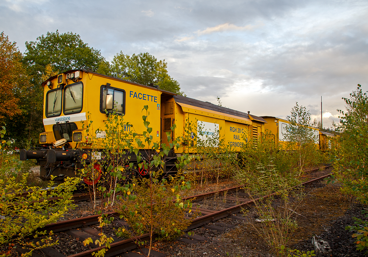 
Die Harsco Track Technologies Gleis- und Weichenschleifmaschine (engl. Rail Grinder) RGH 20 C „Facette“, Schweres Nebenfahrzeug Nr. 99 80 9127 001-2 D-VABWG, der voestalpine BWG GmbH aus Butzbach (Betreiber – EVU: Hessische Güterbahn GmbH) ist am 25.09.2020 in Betzdorf (Sieg) abgestellt, leider etwas im Gebüsch.

Der Schienenschleifzug wurde 2010 von der Harsco Track Technologies (HTT) in den USA unter den Fabriknummern 153635 und 153636gebaut. Das Fahrzeug hat die EBA-Nummer EBA 03C18A003.

Der Schienenschleifzug ist dreiteilig, an beiden Enden befinden sie die selbstfahrende 4-achsige (2 Drehgestelle) 10-Steine-Schienenschleifmaschinen (RGH 10C2-38 bzw. RGH 10C2-39) und dazwischen ein antriebsloser zweiachsiger Mittelwagen. Die selbstfahrende 20-Steine-Schienenschleifmaschine dient zur Beseitigung von Fahrflächenfehlern, Schäden aus Rollkontaktermüdung und der kohlenstoffarmen Randschicht aus dem Walzprozess sowie zur Schienenkopfprofilierung. Der Einsatz erfolgt vorwiegend in Weichen, Kreuzungen und Bahnübergängen ohne Demontage von Ausrüstungsteilen.
Jeder Schleifkopf bestehend aus einem Hydromotor, einer Spindel-Lager-Einheit und einer Schleifscheibe ist unabhängig gelagert und wird einzeln gesteuert, so dass bei 1 Überfahrt 10 verschiedene Facetten geschliffen werden können. Die Winkelstellung, seitliche Position und Sollstellung werden komplett in Schleifabläufen programmiert. 
Der Schleifdruck jeder Scheibe ist einzeln regelbar. Der zulässige Winkelbereich beträgt 75˚ auf der Schieneninnenseite bis 45˚ auf der Schienenaußenseite, gemessen zur Senkrechten. Zur Kontrolle des Ergebnisses ist ein Schienenprofilmesssystem vorhanden.

An beiden Schleifwagen ist eine Staubabsaug und-sammeleinrichtung vorhanden, die Absaugung erfolgt jeweils durch einen Ventilator, der einen Luftstrom von ca. 8.000 m³/h erzeugt. Beide Schleifwagen verfügen zudem über eine integrierte Feuerlöschanlage.

Technische Daten:
Spurweite: 1.435 mm
Achsfolge: Bo’Bo’ + 2 + Bo’Bo’
Anzahl der Achsen: 10
Länge über Puffer: 41.738 mm (13,94 / 13,85 / 13,94 m)
Breite: 2.629 mm
Höhe über SOK: 3.928 mm
Gesamtgewicht: 124 t
max. Achslast: 15 t (Zul. Streckenklasse A und höher)
Höchstgeschwindigkeit (Eigen / Schlepp): 100 km/h
Kleister befahrbarer Gleisbogen: R 90 m
Zur Mitfahrt zugel. Personen: 5
Max. Anhängelast: 50 t

Schleifspezifische Kennwerte:
Aufstelllänge vor Schleifbeginn: 60 m
Geräuschentwicklung (25 m Abstand): 73 dbA
Schleifgeschwindigkeit: 3 bis 8 km/h
Schleifrichtungen: 2 
Drehzahl der Schleifmotoren: 5.500-6.000 min-1
Leistung der Schleifmotoren: 17 kW
Schleifscheiben: Topfscheibe (16 Stück) Ø 152 mm und Tellerscheibe (4 Stück) Ø 280 mm
