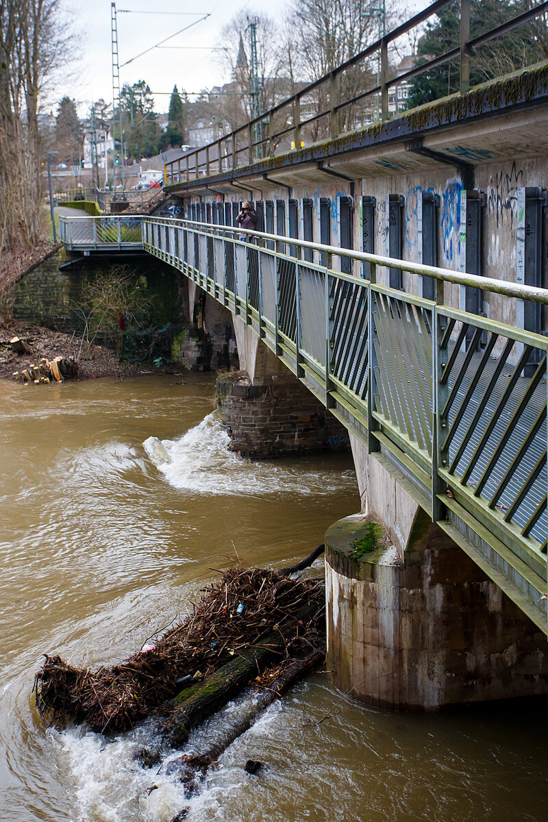 Die vom Hochwasser beschädigte Eisenbahn-Siegbrücke mit Fußgängersteg in Kirchen (Sieg), der Siegstrecke (KBS 460), hier am 03.01.2024.

Die Bahnstrecke Siegen - Köln wird zwischen Kirchen und Betzdorf bis min. Ende nächster Woche gesperrt bleiben. Das hat die Deutsche Bahn Dienstagnachmittag mitgeteilt. Durch das Sieg-Hochwasser gibt es Schäden an einer Eisenbahnbrücke in Kirchen (kurz vorm Bahnhof). Aufgrund der Wetterlage und der weiterhin anhaltenden Regenfälle sei die Sperrung erforderlich, so die Bahn-Pressestelle. Die Züge des RE 9 können wegen der Streckensperrung nur bis Betzdorf fahren. Zwischen Siegen und Kirchen verkehrt die Regionalbahn 90 der Hessischen Landesbahn, leider aber nur wenige und teils mit „kleinen“ LINT 27 Triebwagen. Da wäre wahrhaft mehr möglich und man müsste den SEV nur zwischen Betzdorf und Kirchen betreiben. Aber aufgrund aktuell hoher Krankenstände kommt es auf der Linie RE 9 zudem zu Einschränkungen bis 12.01.2024.

Ich konnte mir den Schaden an einen Brückenpfeiler selbst anschauen (Bilder folgen) und finde die Streckensperrung richtig, darüber ließ ich auch keinen mit Personen besetzten Zug fahren. Was wäre wenn ein Zug darüber fährt und dadurch einbricht. Wer will das verantworten!!! 

Am 29.12.2023 wollten wir mit der Bahn nach Siegen, durch die Reiseauskunft unter www.bahn.de sahen wir bereits das durch wegen einer beschädigten Brücke zwischen Betzdorf (Sieg) und Kirchen (Sieg) ist eine Brücke beschädigt. Die Züge der Linie RE9 aus Richtung Köln enden und beginnen demnach in Betzdorf (Sieg). Die Züge der Linie RE 9 aus Richtung Siegen Hbf enden und beginnen demnach in Kirchen, diese waren aber nicht zu sehen. Bis dahin gab es keine Informationen zur Dauer der Sperrung. Somit fuhren wir mit dem Auto nach Kirchen und fuhren dann mit der RB 90 der HLB (Hessischen Landesbahn) in einem LINT 27, wie die Ölsardinen, nach Siegen Hbf. Auf der Rückfahrt um 14:31 Uhr (ab Siegen) mit RB 90 fuhren wir in einem LINT 41.

Am 30.12.2023 fuhren wir nochmal nach Siegen, das Wetter war besser und unser Ticket war noch gültig. Die Rückfahrt von Siegen machten wir um 13:31 Uhr mit dem HLB RB 90 nach Altenkirchen, dem HLB VT 261 einem LINT 41, dieser war der erste Zug der wieder durchfuhr und die Brücke in langsamer Fahrt befuhr. 

Später hieß es: Die Brücke zwischen Betzdorf und Kirchen ist nach wie vor beschädigt. Die Strecke ist aber wieder befahrbar. Die Züge fahren in dem betroffenen Streckenabschnitt langsamer. Reisende müssen mit Verzögerungen rechnen und sollten ihre Reiseverbindung kurz vor der Abfahrt des Zuges überprüfen.

Nun ist aber der betroffene Streckenabschnitt wieder gesperrt, die Brücke kann nicht mehr befahren werden.
