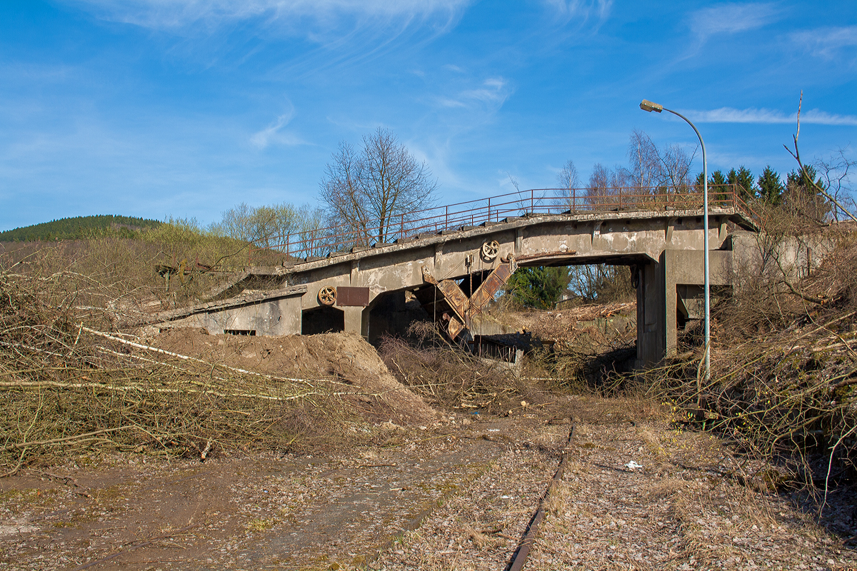 Die letzten Reste der Bremsbahn der Eiserfelder Steinwerke AG des Basaltbruches Mahlscheid (Mahlscheiderkopf). Die ehemalige Verladestation am 24.03.2011 (im gleichen Jahr angerissen) bei der alten Ziegelei in Herdorf.

Der ehemalige Steinbruch Mahlscheid (heute NSG) befindet sich im Westerwald an der Landesgrenze der Bundesländer Rheinland-Pfalz und Nordrhein-Westfalen im Bereich der Gemeinden Herdorf (Landkreis Altenkirchen) und Struthütten (Landkreis Siegen-Wittgenstein). Mitten durch den ehem. Steinbruch verläuft die Landesgrenze, so wurde der Bruch von zwei Firmen betrieben, zum einen auf der Herdorferseite (zu RLP) von der Firma Klein und zum anderen auf der Struthüttenerseite (zu NRW) von den Eiserfelder Steinwerke AG. Von beiden Brüchen führten Bremsbahnen hinab ist Tal. Die der Eiserfelder Steinwerke AG, war ca. 1,5 km lang und führte entlang der Landesgrenze nach hier hinab zur alten Ziegelei, wo das Gestein (Schotter) auf normalspurige Bahnwagen umgeladen wurde. Dafür führte vom Bahnhof Herdorf ein Anschlussgleis hinauf. 

Was ist eine Bremsbahn:
Eine Bremsbahn ist im Grunde eine Standseilbahn, aber ein sehr energiesparendes Konzept, zwei Wagen sind über ein Drahtseil verbunden, welches über eine Bremshaspel führt und kontrolliert abgebremst wird. Das zu fördernde Material wird mittels eines gebremsten Wagens hinabbefördert und der beladene schwererer Wagen zeiht somit den leeren Wagen wieder hinauf. Das Gewicht der zu Tal laufenden beladenen Wagen brachte einfach die dafür nötige Energie auf - also ein sehr energiesparendes Konzept.

Ob die Bremsbahn zwei parallel verlaufende Schienenstränge oder eine abtsche Weiche hatte, ist mir z.Z. nicht bekannt.

