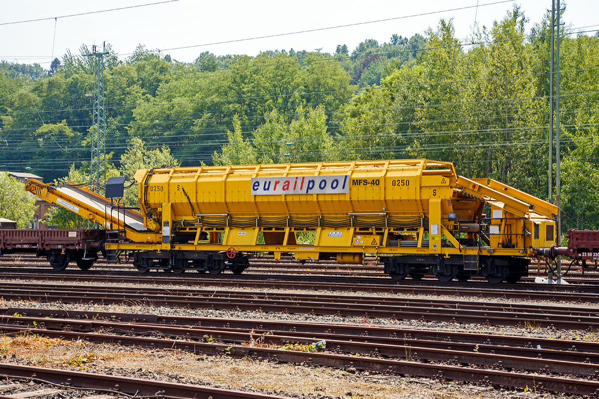 
Die Plasser & Theurer Materialf�rder- und Siloeinheit MFS 40 Nr. 0250 der eurailpool GmbH,  Schweres Nebenfahrzeug Nr. 99 80 9 552 011-5 abgestellt am 04.07.2015 in Betzdorf/Sieg.

Die Materialf�rder- und Siloeinheiten dienen sowohl der Materialversorgung als auch zum Abtransport der Aushubmassen ohne Benutzung des Nachbargleises. Die Beladung erfolgt mittels Radlader oder Bagger �ber eine Beladestation oder direkt in die MFS. Der Abraum wird �ber schwenkbare F�rderb�nder auf Zwischenlagerpl�tze oder K-Wagen entladen.

Technische Daten:
Spurweite: 1.435 m
Anzahl der Achsen: 6 in 2 Drehgestellen
L�nge �ber Puffer: 18.300 mm
Drehzapfenabstand: 11.000 mm
Achsabstand im Drehgestell: 3.400 mm
Fassungsverm�gen: 40 m�
Eigengewicht: 37 t
Nutzlast: 53 t
Motorleistung:  50 kW (f�r Antrieb der F�rderb�nder)
H�chstgeschwindigkeit: 100 km/h (geschleppt)
