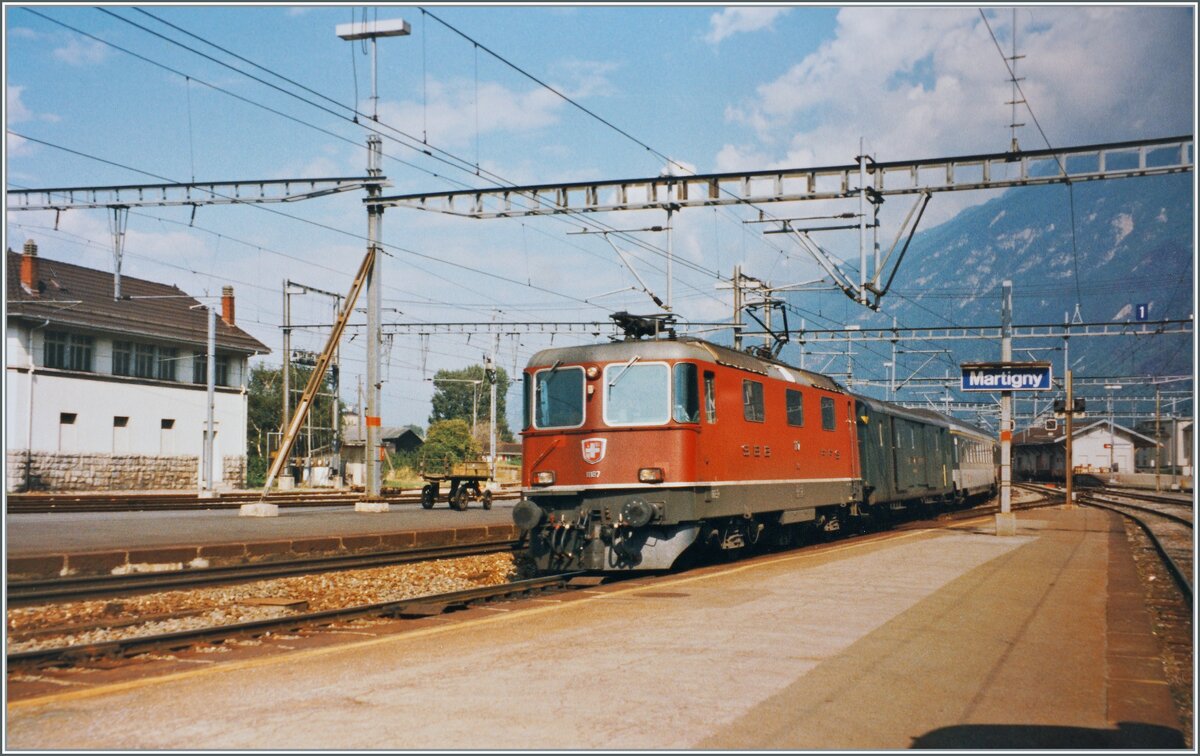 Die SBB Re 4/4 II 11187 verlässt mit einen Schnellzug den Bahnhof von Martigny. Der Schnellzug ist auf der Fahrt von Brig nach Basel SBB via Lausanne und Biel/Bienne. Analogbild vom August 1995