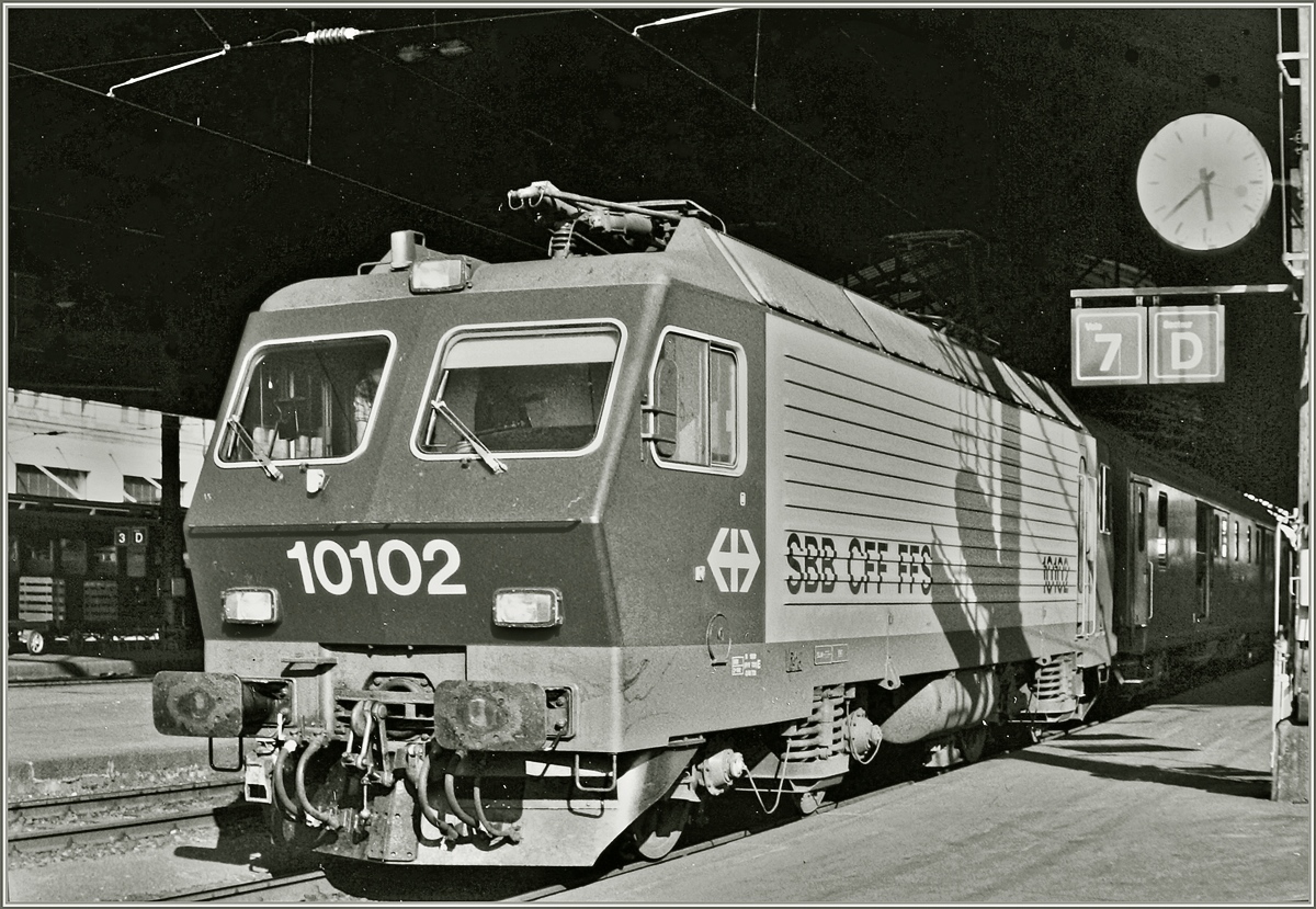 Die SBB Re 4/4 IV 10102 mit einem internationalen Schnellzug (wahrscheinliche Milano - Genève), wie am Gepäckwagen hinter der Lok zu erkennen ist beim Halt in Lausanne. 
Das Anlalog-Bild wurde 1985 aufgenommen.