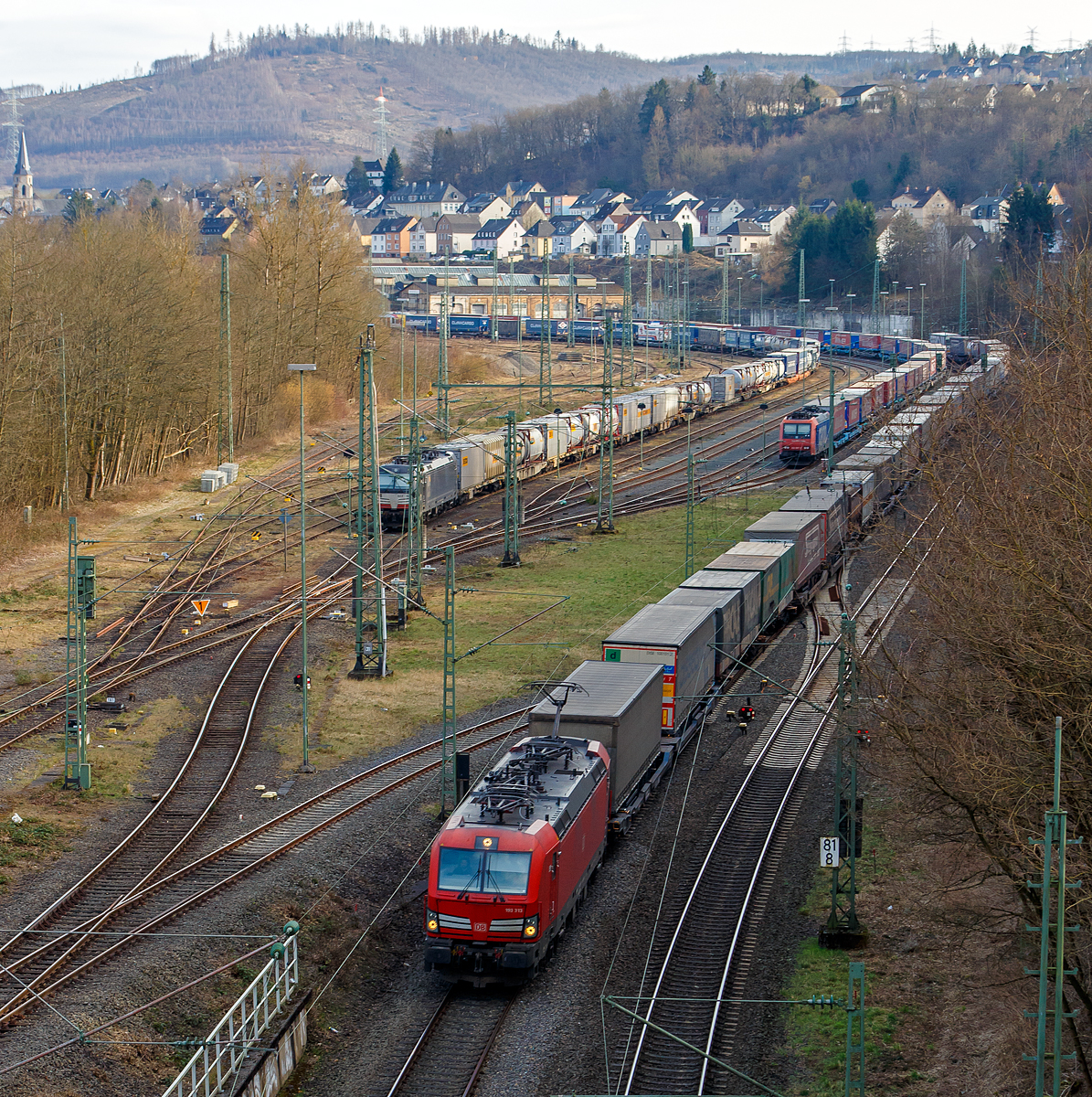 Durch die Sperrung der rechten Rheinstrecke bei Bonn-Beul ist die Woche wieder viel Umleiterverkehr auf der Siegstrecke....
Hier am 12.03.2022 ein Blick von der Brücke in Betzdorf-Bruche auf den Rangierbahnhof Betzdorf/Sieg und die Siegstrecke. Rechts auf der Siegstrecke fährt die 193 313 (91 80 6193 313-4 D-DB), eine Siemens Vectron MS, der DB Cargo AG mit einem KLV-Zug in Richtung Köln. Während im Rbf links die an die DB Cargo vermietete Siemens Vectron MS der MRCE Dispolok, die X 4 E – 701 / 193 701-0 (91 80 6193 701-0 D-DISPO) mit einem Container-/KLV-Zug und rechts davon die SBB Cargo AG Re 482 007-2 (91 85 4482 007-2 CH-SBBC) mit einem „Winner“-KLV-Zug abgestellt sind. 

Die DB Cargo 193 313 eine Vectron MS wurde 2018 von Siemens in München-Allach unter der Fabriknummer 22414 gebaut und an die DB Cargo geliefert. Diese Vectron Lokomotive ist als MS – Lokomotive (Multisystem-Variante) mit 6.400 kW konzipiert und zugelassen für Deutschland, Österreich, Schweiz, Italien und Niederlande (D/A/CH/I/NL), sie hat eine Höchstgeschwindigkeit von 200 km/h. So ist es möglich ohne Lokwechsel vom Mittelmeer die Nordseehäfen Rotterdam oder Hamburg an zu fahren.