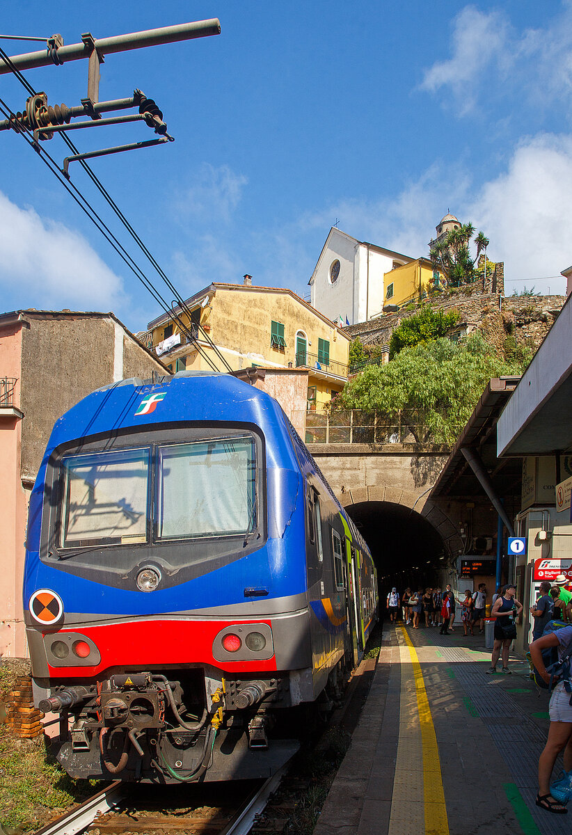 Ein Trenitalia Doppelstockzug (gezogen von einer E.464) hat am 22.07.2022, als Cinque Terre Express (Regionale) von La Spezia, via Riomaggiore, Manarola, Corniglia, Vernazza, Monterosso, nach Levanto, den Cinque Terre Bahnhof Vernazza erreicht. 

Vernazza ist eines der fünf Dörfer der Cinque Terre (Fünf Ortschaften) und verfügt, wie die anderen Dörfer, über einen Bahnhof an der Bahnstrecke Pisa–Genua (RFI Strecke-Nr. 77 / KBS 31 La Spezia–Genua). Der Bahnhof liegt zwischen zwei zweigeteilten Tunneln, jeder Bahnsteig hat seine eigenen Tunnelröhren. Wie auch in Riomaggiore passen die Bahnsteige nicht komplett unter freien Himmel, der Rest der Bahnsteige ist jeweils in einem der Tunneln. 

Oben die Kirche San Francesco (Chiesa di San Francesco) vom gleichnamentlichen Kloster Convento di San Francesco, welches hinter der Kirche liegt.
