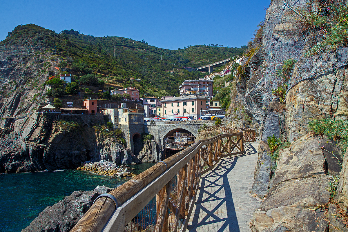 Ein Trenitalia Frecciargento ETR 485 (Pendolino) fährt am 22.07.2022 durch den Bahnhof Riomaggiore in Richtung Genova, während in gleicher Fahrtrichtung ein „pop“ (ETR 103) als Cinque Terre Express den Bahnhof erreicht. Es war wohl eine Überholfahrt des ETR 485.

Riomaggiore ist das südlichste der fünf Dörfer der Cinque Terre (Fünf Ortschaften) an der Italienischen Riviera und verfügt, wie die anderen Dörfer, über einen Bahnhof an der Bahnstrecke Pisa–Genua, die den Ort mit den Nachbardörfern und mit La Spezia und Levanto verbindet. Der Bahnhof von Riomaggiore liegt am nordwestlichen Ortsrand, nur drei bis vier Wagenlängen befinden sich unter freiem Himmel, der Rest der Bahnsteige ist in den beiden Tunneln (davor und dahinter). Der Ortskern wird mittels eines in einem Eisenbahntunnel verlaufenden Fußpfades angebunden.
