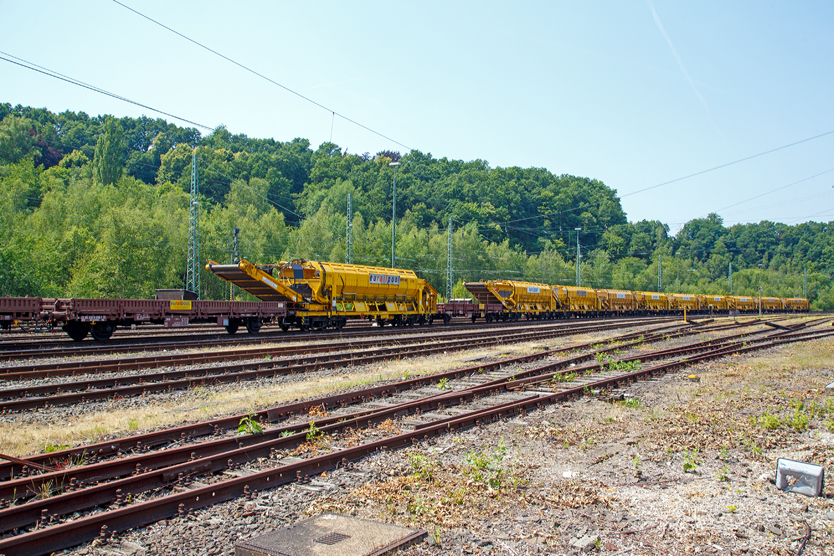 
Ein Zug mit Plasser & Theurer Materialf�rder- und Siloeinheiten MFS 40 der eurailpool GmbH abgestellt am 04.07.2015 in Betzdorf/Sieg.

Arbeitsweise:
Am Boden jedes MFS 40 befindet sich ein �ber die ganze Wagenbreite gehender F�rdergurt und an der Stirnseite ein breites Abgabef�rderband.

Das Aushubmaterial f�llt von der Maschine kommend auf den Bodengurt, wird zum Abgabef�rderband gebracht und an die n�chste Einheit �bergeben. Dieser Vorgang wiederholt sich, bis die am weitesten entfernte Siloeinheit erreicht wird. Bei dieser vordersten Siloeinheit ist das Abgabef�rderband an der Stirnseite des Wagens in Ruhestellung.

Auch der F�rdergurt am Boden des Wagens ist so lange in Ruhestellung, bis die obere F�llgrenze erreicht ist. Dann wird der F�rdergurt in Bewegung versetzt und dadurch im �bergabebereich freier Raum f�r die weitere Beladung geschaffen. Durch die dem F�lltempo angepasste Geschwindigkeit des F�rdergurts wird die ganze Siloeinheit vollst�ndig gef�llt. Das Fassungsverm�gen einer Siloeinheit betr�gt 40 Kubikmeter.

Nach F�llung einer Teilgruppe des Abraumzuges kann diese von der Restgruppe abgekuppelt werden, zu einer Entladestelle gefahren und dort entleert werden, w�hrend die Restgruppe des Abraumzuges noch bef�llt wird. Das Entladeband ist nach beiden Seiten ausschwenkbar. Die Entladung kann dabei auf einer Deponie erfolgen oder es k�nnen LKW's oder Waggons am Nachbargleis beladen werden. S�mtliche Einheiten des Abraumzuges k�nnen durch Ausschwenken aller Abgabef�rderb�nder gleichzeitig entleert werden. Die Entladung eines Wagens dauert ungef�hr f�nf Minuten.
