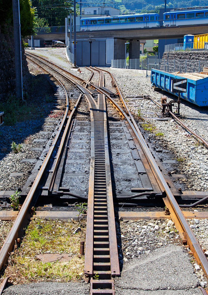
Eine konventionelle Zahnstangen- Zungenweichen (Zahnstangensystem Riggenbach) durchgehend mit Riggenbach-Zahnstange versehene Weiche der Rigi-Bahnen beim Depot Arth-Goldau am 23.06.2016.

Da sich die fertige Riggenbach-Zahnstange nicht biegen l�sst, ist die Weiche mit beweglichen Zahnstangenelementen ausger�stet, damit die Zahnstangen des einen Strangs die Schienen des andern Strangs kreuzen k�nnen. Weil damit ein ununterbrochener Zahnradeingriff gew�hrleistet ist, k�nnen sie auch auf geneigten Strecken eingebaut werden.

Der Vorteil von Zungenweichen mit Zahnstange gegen�ber klassischen Schleppweichen mit verschiebbarem Gleisrost sind die nur geringen temperaturbedingten L�ngen�nderungen der kurzen beweglichen Zahnstangenteile. Nennenswerte Teilungsfehler k�nnen durch Temperatur�nderungen nicht auftreten.

Das Zahnstangensystem Riggenbach:
Bei der von Niklaus Riggenbach 1863 in Frankreich patentierte Leiterzahnstange werden zwischen zwei U-Profilen die Z�hne als Sprossen eingesetzt. Urspr�nglich waren sie genietet, heute werden sie geschwei�t. Diese Bauart zeichnet sich aus durch trapezf�rmige Z�hne, was Evolventenverzahnung und damit eine konstante Kraft�bertragung erm�glicht. Untersuchungen zeigten, dass die eingef�hrte Zahnform optimal war. Deren Flankenwinkel wurden auch f�r die sp�teren Zahnstangenbauarten �bernommen. Die Riggenbach-Zahnstange ist wegen ihrer massiven Konstruktionsweise robust, l�sst sich mit einfachen Mitteln fertigen und erreicht die zweitgr��te Verbreitung aller Systeme.

Bei den 1871 bis 1875 in Betrieb genommenen Bahnen auf die Rigi ragen wie beim System Marsh (Leiterzahnstange mit Z�hnen aus Rundprofil) die Zahnr�der unter die Schienenoberkante.

Da sich die fertige Zahnstange nicht biegen l�sst, m�ssen die Zahnstangenelemente genau f�r den jeweils ben�tigten Radius hergestellt werden. Eine Zahnstangenstrecke wird deshalb so geplant, dass sie mit m�glichst wenigen Grundelementen erstellt werden kann. 
