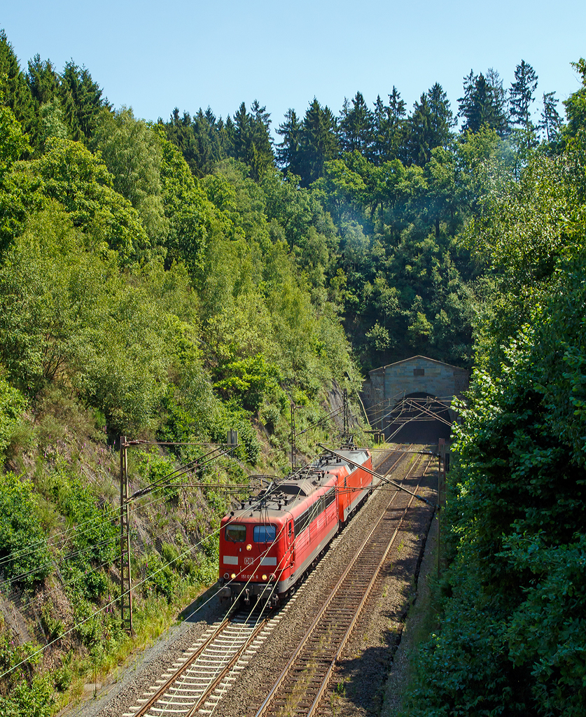 
Genau 100 Jahre nach Fertigstellung kommen sie aus dem Tunnel.... 

Die 151 029-6 (91 80 6151 029-6 D-DB) und 152 167-3 (91 80 6152 167-3 D-DB) der DB Schenker Rail Deutschland haben gerade (am 02.07.2015) gemeinsam als Lz den 2.652m langen Rudersdorfer Tunnel verlassen und fahren Richtung Norden. 
Einen lieben Gruß an den freundlichen Lokführer zurück.

Der Rudersdorfer Tunnel ist ein 2.652 m langer Eisenbahntunnel der Dillstrecke (KBS 445) zwischen Siegen und Haiger. Als Hauptingenieurbauwerk des nördlichen Abschnitts dieser Bahnstrecke durchsticht er die Tiefenrother Höhe (552,3 m), einem Berg des Rothaargebirges auf der Grenze von Nordrhein-Westfalen und Hessen.

Aufgrund der schwierigen Topografie und der begrenzten technischen Möglichkeiten war eine direkte Verbindung zwischen Siegen, Haiger und Dillenburg zum Zeitpunkt des Baus der Deutz-Gießener Bahn vom heutigen Köln-Deutz nach Gießen in den 1850er Jahren noch nicht möglich. Erst 1915 wurde die direkte Verbindung zwischen Siegen und Haiger fertiggestellt. Am 2. Juli 1915 endeten auch die Arbeiten am Tunnel, das sind nun genau 100 Jahre her.