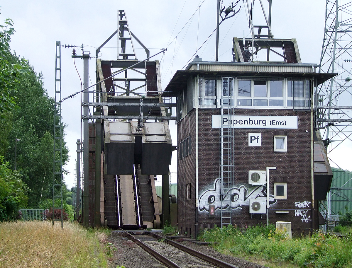 
Gleich vor dem Bahnhof Papenburg (Ems) befindet sich die Eisenbahnklappbrücke über den Papenburger Sielkanal, davor noch das Fahrdienstleiterstellwerk Papenburg (Ems) „Pf“, hier am 20.06.2009.

Die beiden Brückenteile werden gerade wieder abgesenkt.