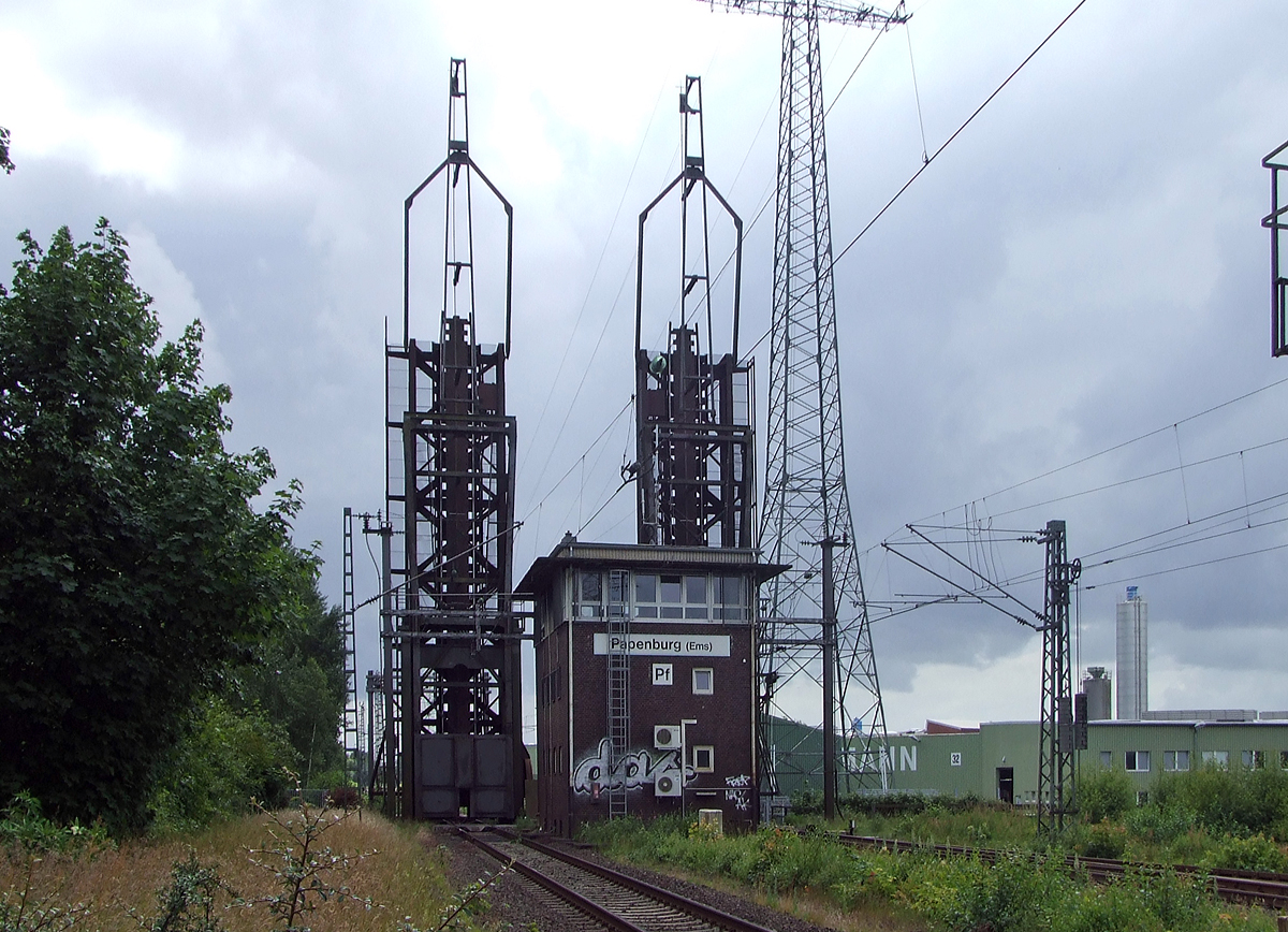 
Gleich vor dem Bahnhof Papenburg (Ems) befindet sich die Eisenbahnklappbrücke über den Papenburger Sielkanal, davor noch das Fahrdienstleiterstellwerk Papenburg (Ems) „Pf“, hier am 20.06.2009.

Hier ist die Brücke, für die freie Schiffsdurchfahrt, gerade oben.