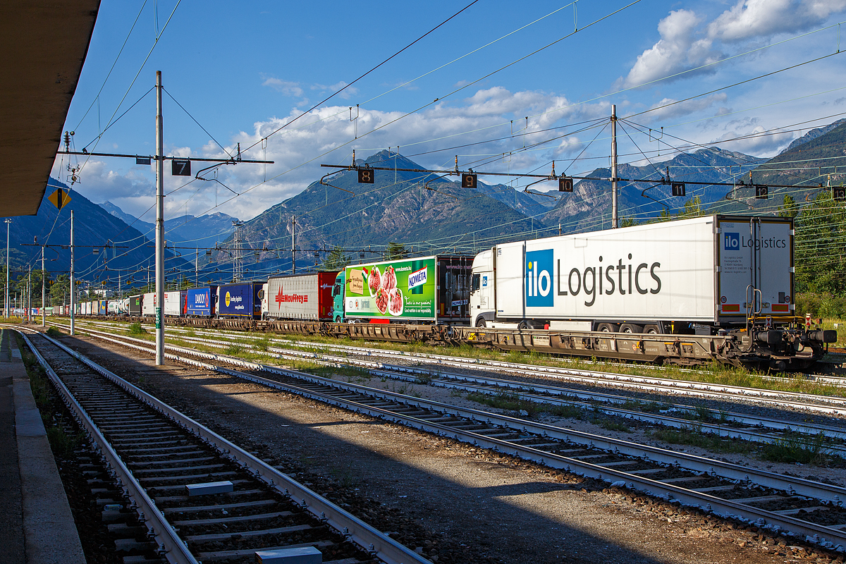 Hier kann man die komplette L�nge des RoLa-Zug (Rollende Landstra�e) sehen...
Die an die SBB Cargo International AG vermietete Vectron 193 478-5  Gottardo  (91 80 6193 478-5D-SIEAG) der LokRoll AG und die SBB Cargo Re 484 017-9 / E 484.017 SR (91 85 4484 017-9 CH-SBBC)  haben am 02.08.2019 mit einem RAlpin-RoLa-Zug aus Novara den Rbf Domodossola erreicht. Die Loks kann man links hinten noch gerade erkennen. Obwohl diese Loks den Zug auch weiter durch Simplon und die Schweiz ziehen k�nnten, die Zulassungen haben sie, �bernehmen gleich zwei BLS Re 485 (TRAXX F140 AC1) den Zug. 

Diese Rola-Z�ge sind f�r den Transport von Last- und Sattelz�gen im begleiteten Verkehr, einer Form des kombinierten Ladungsverkehrs, vorgesehen und kommt in alpenquerenden Shuttlerelationen zum Einsatz. Dabei fahren Lastkraftwagen in speziellen Terminals direkt von der Stra�e �ber eine Rampe auf den Wagen, um vom Ausgangsort zum Ziel transportiert zu werden. Der Fahrer zieht sich in einen speziellen Begleitwagen mit Liegeabteilen zur�ck, f�hrt am Zielort weiter und liefert die Ware sicher beim Kunden ab. Diese Form des kombinierten Verkehrs von Schiene und Stra�e – Rollende Landstra�e (ROLA) – gewinnt, nicht zuletzt aufgrund von gesteigertem Verkehrsaufkommen und Umweltbewusstsein, immer mehr an Bedeutung.

Auch in Deutschland (in Nordrhein-Westfalen) denkt man �ber Rola-Z�ge nach, der Grund liegt aber darin, dass eine Talbr�cke der Autobahn A 45 im Raum L�denscheid nicht mehr befahrbar ist. Ein Neubau dauert bekanntlich Jahre, so bleibt auf Jahre hin die Umleitungsstecke �ber Landstra�en (durch L�denscheid) �berlastet.

