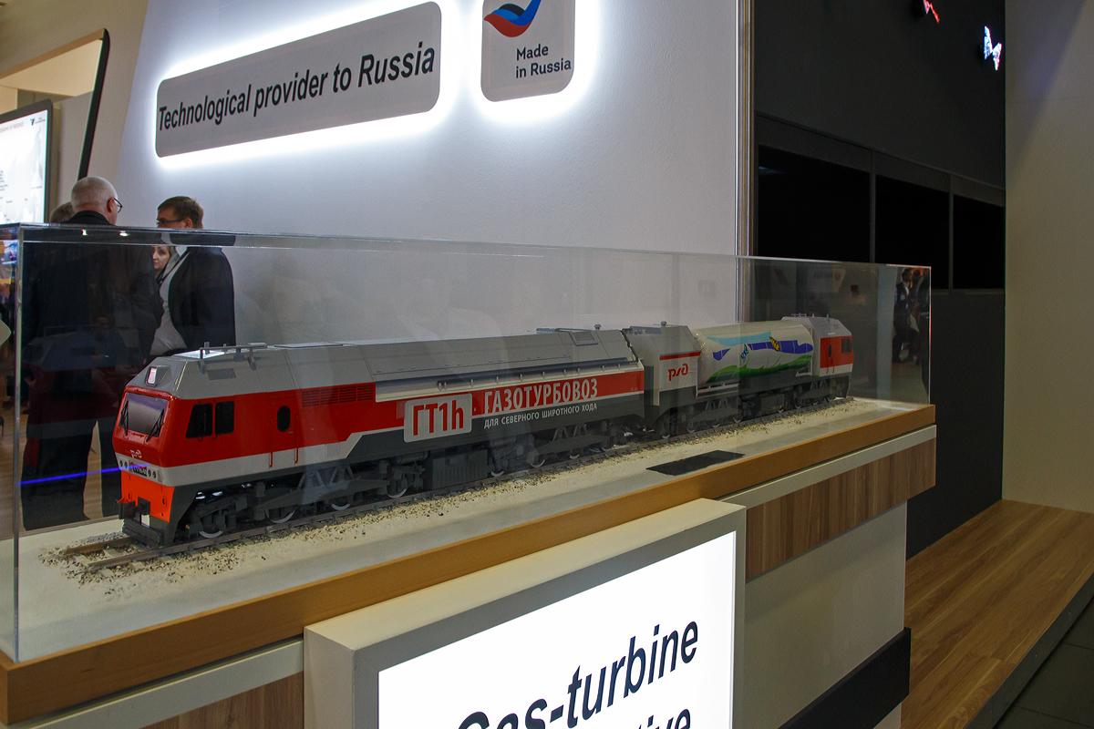 Leider nur als Modell ausgestellt auf der InnoTrans 2018 (hier 18.09.2018) die mächtige 16-achsige russische RŽD Gasturbinen-Lokomotive  ГT1h-002 (GT1h-002).

Die Lokomotiven der RŽD-Baureihe ГT1h (deutsche Transkription GT1h) der Russischen Eisenbahnen (RŽD) sind schwere Gasturbinenlokomotiven mit elektrischer Kraftübertragung, vorrangig für den Güterzugdienst. Sie sind bestimmt für den schweren Güterzugdienst auf nichtelektrifizierten Abschnitten, vorrangig in Sibirien. Bisher wurden zwei Fahrzeuge gebaut, mit denen umfangreiche Versuche durchgeführt wurden. Die Kraftübertragung geschieht von einer Gasturbine aus, die mit verflüssigtem Erdgas betrieben wird, an ihr ist ein Wechselstrom-Generator angeschlossen, der produzierte Strom wird gleichgerichtet für die Speisung der Traktionsfahrmotoren verwendet. Es ist eine Serie von 40 Fahrzeugen bestellt.

Die Leistung der ГT1 beträgt 8.300 kW, damit gilt die Lokomotive als die leistungsstärkste Gasturbinenlokomotive der Welt. Die überarbeitete ГТ1h.002 besitzt eine Anfahrzugkraft von 980 kN, die Zugkraft im Dauerleistungs-Regime (bei 33 km/h) beträgt 775 kN.

Die Ausarbeitung begann im 2005 nach der Unterzeichnung des Vertrages zwischen der RŽD und der All-Russian Rolling Stock Design and Technology Research Institute. Spezialisten der Kompanie Kusnezow schufen die starke Gasturbine НК-361 (NK-361) und den Antriebsblock der Gasturbinenlok. 2007 entstand die erste Versuchslokomotive, die auf der Basis der ВЛ15.008 hergeleitet wurde. Die Gasturbine entstand in Samara, die Montage der Lokomotive wurde in dem Ausbesserungswerk Woronesch durchgeführt. Die neue Lokomotive bekam die Bezeichnung ГT1-001 zuerkannt. Die Lokomotive hat eine Dienstgewicht von 300 t und einen Kraftstoffvorrat von 17 Tonnen. 
Am 4. Juli 2008 beförderte die ГT1-001 zum ersten Mal eine Güterzugeinheit. Die Masse des Zuges betrug 3.000 t, und die Überprüfung wurde auf dem Abschnitt Kinel–Schigulewskoe More der Eisenbahn im Oblast Kuibyschew durchgeführt. Damals war geplant, dass die ersten Gasturbinenloks in Sibirien zum Einsatz kommen werden, wo die meisten Vorkommen von Erdgas lagern. Am 22. Dezember 2008 fuhr sie zum ersten Mal einen Güterzug mit einer Masse von 10.000 t, bestehend aus 116 Wagen. Ein Güterzug mit einer Masse von 15.000 t, bestehend aus 159 Wagen wurde zum ersten Mal am 23. Januar 2009 gefahren. 
Am 12. Oktober 2009 erhielt die RŽD im Guinness-Buch der Rekorde ein Diplom für den Bau der leistungsstärksten Gasturbinenlok der Welt, die mit verflüssigtem Erdgas angetrieben wird. 
Am 7. September 2011 fuhr auf dem Gleisring des VNIIZhT in Schtscherbinka ein Güterzug mit einer Masse von 16.000 t, bestehend aus 170 Wagen, was einige Institutionen in Russland fehlerhaft als Weltrekord auslegten. 
Im Jahr 2012 erfolgte, mit dem Ersatz der Diesel-Krafteinheit für die Erstellung der Hilfsenergie durch eine Akku-Batterie, eine Modernisierung. Seit der Zeit besitzt die Lokomotive den Index h (hybrid). 
Ab August 2013 lieferte die Diesellokfabrik Ljudinowo eine Serienausführung der Gasturbinenlokomotive aus, die die Bezeichnung ГT1h-002 erhielt. Die Serienausführung hat eine Dienstgewicht von 368 t und einen Kraftstoffvorrat von 20 Tonnen.

TECHNISCHE DATEN:
Spurweite: 	1.520 mm (Breitspur)
Achsformel: (Bo’Bo’) (Bo’Bo’) + (Bo’Bo’) (Bo’Bo’
Länge über Kupplung: 2 × 21.500 mm
Drehzapfenabstand:  10.900 mm
Achsstand im Drehgestell:  6.300 mm (3 × 2.100 mm)
Treibraddurchmesser: 	1.050 mm (neu)
Höhe:  5.250 mm
Breite: 3.150 mm
Dienstgewicht: 2×184 t = 368 t
Radsatzfahrmasse:  23,5 t 
Leistung: 8.300 kW
Dauerleistung: 6.458 kW
Anfahrzugkraft: 980 kN
Dauerzugkraft: 775 kN bei 30 km/h
Höchstgeschwindigkeit: 100 km/h
Motorentyp:  Gasturbine vom Typ  NK-361
Nenndrehzahl: 6.000 U/min
Leistungsübertragung: elektrisch
Tankinhalt:  20 t
Anzahl der Fahrmotoren: 16 Gleichstrommotore
