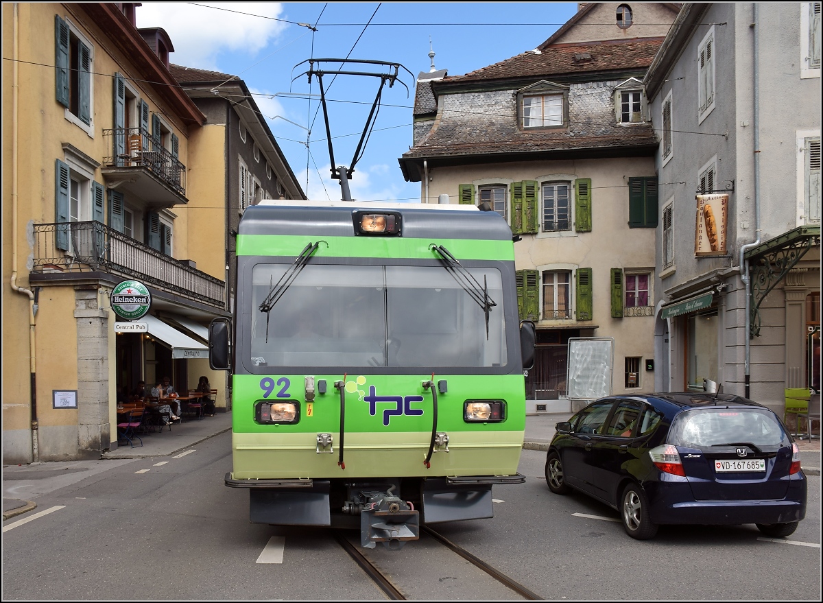 Ortsdurchfahrt in Bex. Das Auto ist in Sicherheit gebracht, es kommt TPC-Triebwagen 92 der Bex–Villars-sur-Ollon–Bretaye-Bahn entgegen. Juli 2017. 