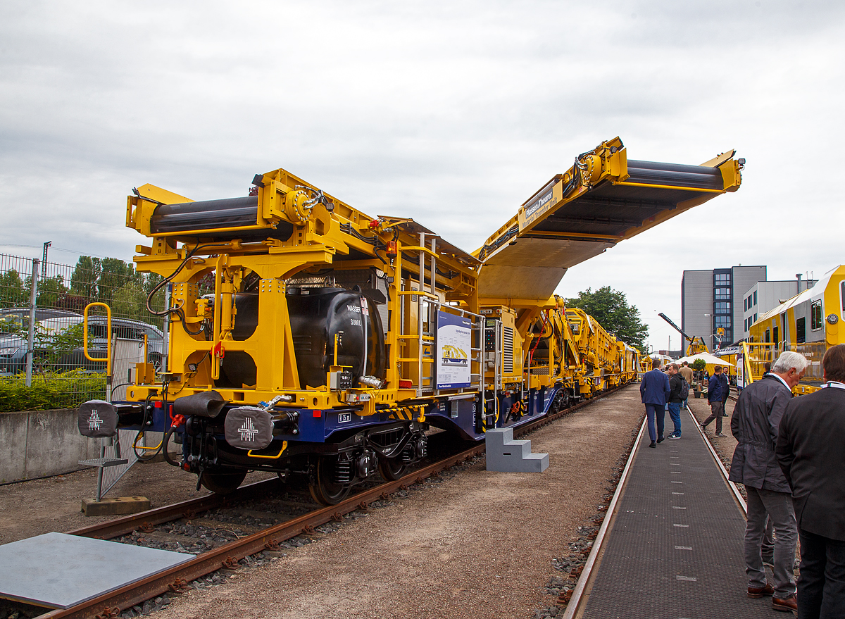 Plasser & Theurer präsentierte auf der iaf 2022 in Münster (hier am 31.05.2022) die Plasser MaterialTransferUnit / Materialfördereinheit aufgebaut auf einen Standard Containertragwagen der Gattung Sgnss 60´ (hier auf 37 81 4565 020-6 A-PLA der Franz Plasser Vermietung von Bahnbaumaschinen GmbH, Purkersdorf). 

Die Maschine wurde 2022 von Plasser & Theurer in Linz (A) unter der Maschine-Nr. 7191 gebaut. Sie ist eine Erweiterung des Materialkreislaufs, für Umladen, Beladen und Durchfördern von Schüttgut

Ausstattung und Aufbau:
• Modularer Aufbau nach Anforderung Umladen, Beladen, Durchfördern
• Flexible Schüttgutlogistik mit großer Abwurfweite ohne äußere Abstützung, Schwenkförderband mit einer Ausladung bis zu 6.870 mm, Transportsicherung für Schwenkförderband
• Beladen von Schüttgut durch konventionelle Baumaschinen, wie Bagger
• Durchfördern von Schüttgut in der MFS-Förderstraße mit Funktionsraum
• Modularer Aufbau auf Standard Containertragwagen (Sgns 60') als Trägerfahrzeug und Modultragrahmen 20´
• Autarke Energieversorgung zur flexiblen Einreihung  in eine Förderstraße, u.a. mittels Dieselmotor EURO V und Hydrauliknotpumpe
• Durchgehende selbsttätige Bremse
• Aufstieg mit Geländer
• Funkfernsteuerung für Schwenkförderband
• LED-Beleuchtung
• Funktionsraum mit Sozialeinrichtung
• Wassersprühanlage zur Staubreduktion
• Wassertank 3.000 1
• Zugwarnanlage mit Druckluft-Warnanlage System Zöllner
• Werkzeugschrank

TECHNISCHE DATEN:
Spurweite: 1.435 mm (Normalspur)
Anzahl der Achsen:  4 in 2 Drehgestellen
Länge über Puffer: 19.740 mm
Drehzapfenabstand: 14.200 mm
Achsabstand im Drehgestell: 1.800 mm
Eigengewicht Modul: 52.600 kg
Eigengewicht Tragwagen: 25.800 kg
Max. Achslast: 20 t
Höchstgeschwindigkeit: 100 km/h
Zugelassen für Streckenklasse: C2 oder höher
Kleister befahrbarer Gleisbogen: R 75 m
Bremse: KE-GP-A (K)
Bremssohle: J 816 M
Handbremse: Ja
Ausladung Schwenkförderband bis zu: 6.870 mm

Die Einheit wurde hier auch so präsentiert wie sie eingereiht werden könnte, dahinter (in Arbeitsrichtung davor) sieht man eine Materialförder- und Siloeinheit MFS 120 und Bettungsreinigungsmaschine RM 85-750 N.