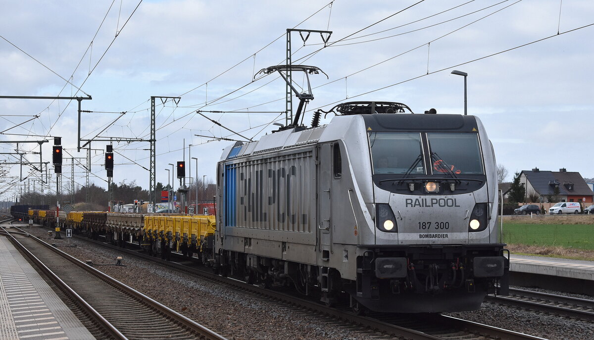 Railpool GmbH, München [D] mit der  187 300-9  [NVR-Nummer: 91 80 6187 300-9 D-Rpool], aktuelle Vermietung? mit einem Transportzug mit Drehgestell-Flachwagen + am Ende Langschienen am 24.02.26 Höhe Bahnübergang Rodleben.
