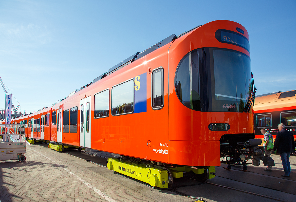 
Stadler Rail pr�sentierte auf der InnoTrans 2018 (hier 18.09.2018) den neuen Worbla-Zug Be 4/10 f�r die RBS (Regionalverkehr Bern-Solothurn),  hier in Form von dem RBS Be 4/10 Worbla 02.  Bis 2020 sollen alle Mandarinli durch die Worblas bei der RBS ersetzt werden.
Der Triebzug steht hier auf Rollb�cke der RailAdventure GmbH („Loco Buggies“).

RBS hat im Juni 2016 bei Stadler in Bussnang 14 vierteilige S-Bahn-Z�ge vom Typ Be 4/10 Worbla (Elektrischer Niederflurtriebzug) f�r die Linie S7 bestellt. Die vierteiligen elektrischen Meterspurz�ge weisen 2 Triebk�pfe am Ende und 3 Jakobs-Laufdrehgestelle als Verbindung zwischen den 4 Wagenk�sten auf. Die Z�ge sind f�r eine maximale Geschwindigkeit von 100 km/h ausgelegt. Sie sind auf der gesamten L�nge von 60 Metern durchgehend begehbar, was die Verteilung der Reisenden im Zug verbessert und das Sicherheitsgef�hl erh�ht. Die Triebz�ge sind klimatisiert und erf�llen die Anforderungen des Behinderten-Gleichstellungsgesetzes. Niederflureinstiege und Schiebetritte zwischen Zug und Bahnsteig erleichtern den Eintritt. Modernste Technologien wie die voll redundante Traktionsanlage inklusive redundanter Leittechnik garantieren eine hohe betriebliche Verf�gbarkeit und tiefe Life-Cycle-Kosten.

Technische Mekmale:
- Niederflurwagen in Alu-Leichtbauweise
- Luftgefederte Trieb- und Jakobslaufdrehgestelle
- Optimierte Motorleistung entsprechend des Einsatzes als Stadtbahn-Triebzug f�r den Betrieb auf Kurzstrecken
- Redundante Antriebsausr�stung (Antriebsstromrichter) in den Endwagen f�r hohe Ausfallsicherheit
- Acht Einstiegst�ren f�r schnellen Fahrgastwechse
- Niederflureintritte an allen T�ren
- T�r-Leuchtmelder (Countdown)
- T�rsensor f�r �handsfree�-Eintritt
- �bersichtliche Plattformen
- Durchgehend begehbar
- Indirekte Beleuchtung
- Gro�z�gige Multifunktionsabteile
- Klimaanlage

TECHNISCHE DATEN:
Bezeichnung: Be 4/10
Name: Worbla
Anzahl Fahrzeuge (geplant): 14
Spurweite: 1.000 mm (Meterspur)
Achsanordnung: Bo‘2‘2‘2‘Bo‘
L�nge �ber Kupplung: 60.000 mm
Fahrzeugbreite: 2.650 mm
Fahrzeugh�he: 3.980 mm
Achsabstand in Drehgestell: 2.000 mm (Triebdrehgestell) / 2.150 mm (Laufdrehgestell)
Trieb- und Laufraddurchmesser: 770 mm (neu)
H�chstgeschwindigkeit: 100 km/h
Max. Leistung am Rad: 4 x 350 kW = 1.400 kW
Anfahrzugskraft: 120 kN (140 kN m�glich)
Anfahrbeschleunigung: 1.0m/s� (1.2m/s� m�glich)
Sitzpl�tze: 130
Stehpl�tze: max. 380
Fu�bodenh�he: 400 mm am Einstieg / 1.000 mm Hochflur
Einstiegbreite: 1 400 mm
Speisespannung: 1.250 V DC

