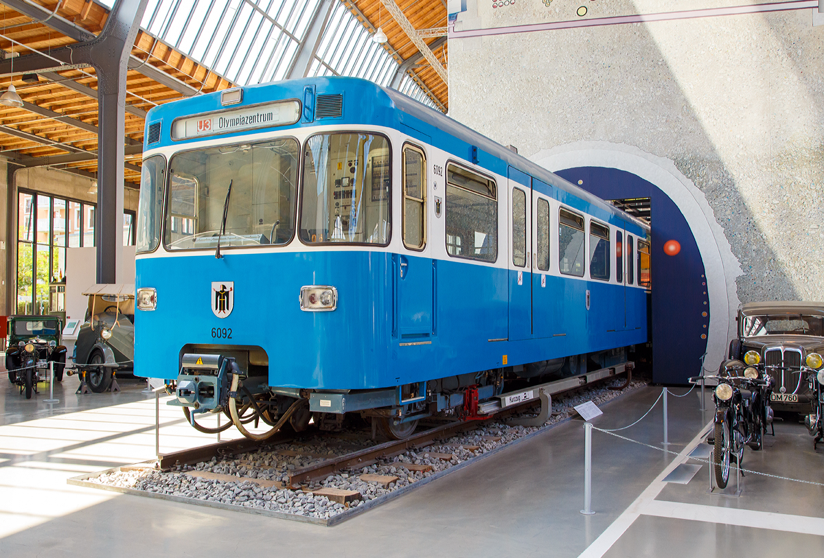 
Triebwagenh�lfte 6 092 (MVG-Baureihe A 1) der ersten M�nchener U-Bahn ausgestellt im Verkehrszentrum des Deutschen Museums (am 16.06.2018) in M�nchen (Theresienh�he).

Am 22.09.1967 wurde der Wagen als eines von drei Prototypfahrzeugen f�r die neue U-Bahn in M�nchen ausgeliefert. Die U-Bahnwagen sind in Leichtbauweise mit Alu-Strangpre�profilen hergestellt worden. Damit konnten hohe Anfahrbeschleunigungen, kurze Bremswege und niedrige Energiekosten erreicht werden. Sechs breite Doppelt�ren auf jeder Seite erm�glichten einen schnellen Fahrgastwechsel. Die Waggon- und Maschinenbau GmbH Donauw�rth (WMD, heute Bombardier Transportation) lieferte insgesamt zwei Prototypen und die Waggonfabrik Josef Rathgeber einen an die damaligen Verkehrsbetriebe der Stadtwerke M�nchen, heute MVG, aus. Zur sp�teren Unterscheidung von den Serienfahrzeugen erhielten sie die Bezeichnung A1.

Die Stromversorgung erfolgte �ber seitliche Stromschienen mit 750 V Gleichstrom. Die elektrische Wagenausr�stung war einfach und robust und bot eine hohe Betriebssicherheit. Ihr geringes Gewicht erg�nzte die Leichtbauweise ideal. Es konnten 2-, 4- und 6 Wagenz�ge aneinander gekuppelt werden. Ein Linienleiter zwischen den Gleisen erm�glichte ein weitgehend automatisches Fahren der Z�ge mit Zielbremsung am Bahnsteig.

Nach erfolgreicher Erprobung der Doppeltriebwagen 6091/7091, 6092/7092 und 6093/7093 erfolgte ab 1970 die Serienauslieferung. Neben den beiden bestehenden Herstellern beteiligten sich zudem MAN sowie O&K am Bau der Fahrzeuge.

Der Wagen 6092 wurde am 28.12.1995 nach 28 Betriebsjahren und 1,31 Millionen km Laufleistung au�er Betrieb genommen und am 01.08.2006 dem Deutschen Museum �bergeben.

TECHNISCHE DATEN (Angaben einer Doppeleinheit):
Spurweite:  1435 mm (Normalspur)
Achsformel: B'B'+B'B'
L�nge �ber Kupplung: 37.150 mm
H�he:  3.550 mm
Breite: 2.900 mm
Drehzapfenabstand:  12.000 mm
Achsabstand im Drehgestell: 2.100 mm
Leergewicht: 51,6 t
H�chstgeschwindigkeit: 80 km/h
Stundenleistung: 4�180 kW = 720 kW
Stromsystem: 750 V Gleichstrom
Sitzpl�tze:  98
Stehpl�tze:  192