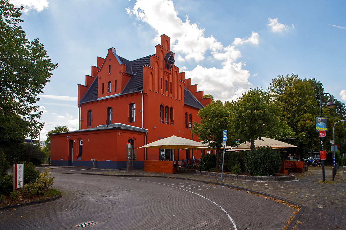 
Von der Straßenseite das Empfangsgebäude des Bahnhofs Schladern (Sieg) an der Siegstrecke im Ort Windeck-Schladern am 07.09.2020. Das im wilhelminischen Stil 1859 erbaute Ziegelgebäude steht unter Denkmalschutz.

Schlosskopie mit eigener Geschichte
Ohne Bahn kein Fortschritt. Erst mit der Bahnlinie zwischen Köln und Gießen durch das Siegtal konnte die Industrie an der Sieg von der wachsenden Wirtschaft der Industrialisierung profitieren. 1860 erhielt Schladern einen eigenen Bahnhof, der schwierigen Streckenführung durch Berge und über den Fluss zum Trotz. Doch der Aufwand lohnte sich, denn Schladern gehörte Damals zum Kreis Waldbröl und sein Bahnhof war bald Hauptumschlagplatz für Waren aus dem Oberbergischen Land. Der Bahnhof mit seinem repräsentativen Empfangsgebäude erinnert dabei auch an eine Zeit, in der man die reiselustigen Großstädter vom Rhein angemessen willkommen hieß. Mit seinem Baustil und den abgestuften Giebeln war die Ähnlichkeit des Baus mit dem ehemaligen Schloss Windeck durchaus gewollt.

Doch obwohl bereits 1870 mit der Gründung der Bröltaler Eisenbahn (Bröltalbahn) zwischen Hennef (Sieg) und Waldbröl (ab 1891 auch ab Bonn-Beuel) ein Großteil des Warenumschlages auf die neue Schmalspurbahn (Spurweite 785 mm) überging, siedelte sich rund um dem Bahnhof Schladern Industrie an: ein Ziegelwerk, ein Eisenwerk und ein großes Kupferwerk mit eigenem Gleisanschuss (zuletzt als Firma „kabelmetal“ bekannt). Mit dem Rückgang des Güterverkehrs auf der Schiene in den 1990er Jahren und dem Aus für „kabelmetal“  nahm die Bedeutung des Bahnhofs Schladern für den Güterverkehr ab, während es für Pendler (meist in den Großraum Köln) immer wichtiger wurde. Das seit 1989 unter Denkmalschutz stehende Empfangsgebäude wurde aufwendig saniert und restauriert.

Quelle: Am Gebäude angebrachte Tafel