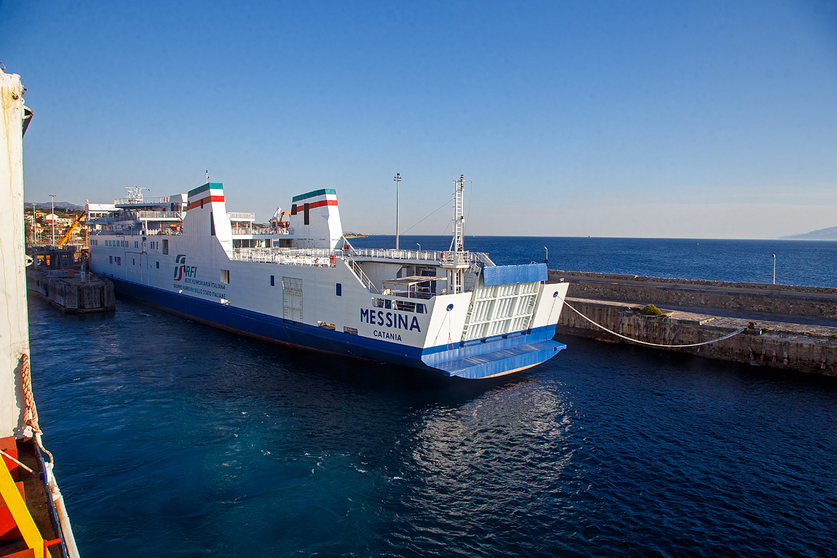Was hat das Schiff (Messina) mit einem Bahnbild zu tun, nun es ist eine Ro-Ro-Eisenbahnfähre und quasi die Bahngleise auf dem Wasser bzw. über die Straße von Messina.....
Die Eisenbahnfähre „Messina“ der RFI Rete Ferroviaria Italiana (zur Gruppe der Ferrovie dello Stato Italiane), liegt für Reparatur- bzw. Wartungsarbeiten am 16.07.2022 am Kai bzw. Mole beim Fährterminal in Villa San Giovanni. Wir sind auf der älteren 1984 gebauten „Villa“.

Das Eisenbahnfähr-Schiff „Messina“ ist neues Flaggschiff des italienischen Eisenbahnnetzes, das für den Transport von Schienenfahrzeugen, Autos und Passagieren in der Straße von Messina bestimmt ist. Es wurde am 29. Juli 2013 in der Straße von Messina in Dienst gestellt. 

Die Fähre Messina-Fähre wurde bei der Werft Nuovi Cantieri Apuania in Marina di Carrara gebaut, die auf den Bau von Ro/Ro-Passagierschiffen spezialisiert ist. Durch einen Streik der Werftarbeiter verzögerte sich der Stapellauf um ca. 3 Monate auf den 7. November 2012. Die Baukosten der Fähre beliefen sich auf 49,5 Millionen Euro.

Die Fähre Messina hat ein viergleisiges Deck und kann wahlweise mit bis zu 138 PKW, 24 LKW, 19 Eisenbahn-Kesselwagen, 27 Güterwagen oder 15 Reisezugwagen beladen werden. Zudem können bis zu 900 Passagiere befördert werden. Die Züge und Wagons werden ausschließlich über die Bugklappe (von vorne) verladen. Straßenfahrzeuge können auch über die Heckrampe oder eine Seitenrampe verladen werden.

Drei achtern angebrachte Azimutstrahlruder, zwei Bugstrahlruder und ein Bugruder erleichtern die Manövrierfähigkeit des Schiffes, Die neue Generation der RFI-Fähren (Messina und Iginia) sind erkennbar am abfallenden Bug und dem Schornsteinpaar (traditionell gibt es nur einen Schornstein bei den Fähren der Staatsbahnen). Beide Schiffnamen gab es bereits schon einmal bei der FS, diese wurden durch die Neubauten Messina (2013) und Iginia (2022) ersetzt. Interessant ist auch das die Tatsache das der Heimathafen der RFI Fähren allgemein Catania ist und nicht wie erwartet Villa San Giovanni oder Messina.

TECHNISCHE DATEN:
Verdrängung: 6.060 t
Bruttoraumzahl : 5.448 BRT
Eigengewicht: 2.710 dwt
Länge: 147 m
Breite: 18,7 m
Geschwindigkeit: 18,7 Knoten (34,63 km/h)
